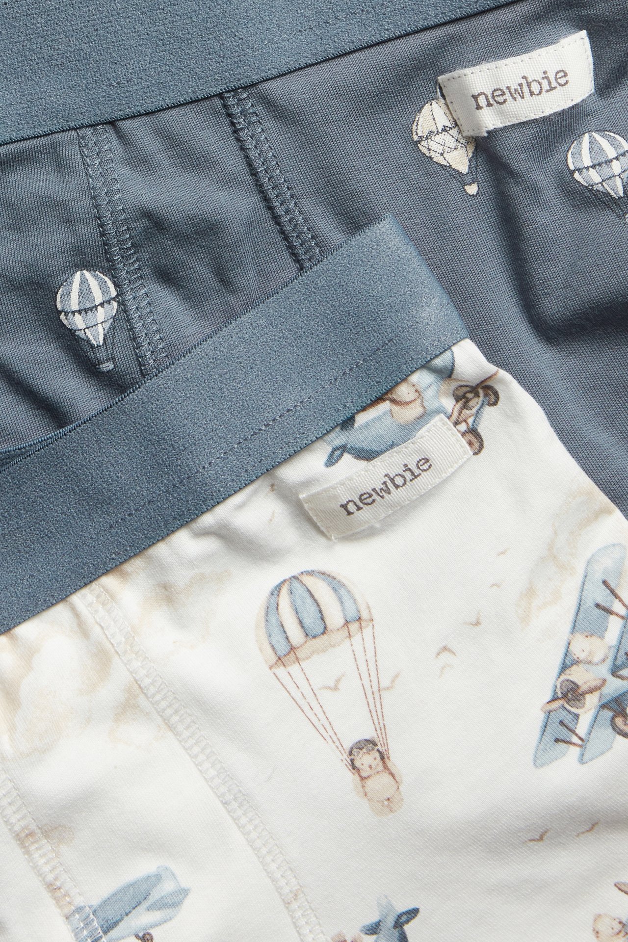 Close-up of kid's two-pack boxer briefs: one off-white with airplanes, one blue-grey with hot air balloons.