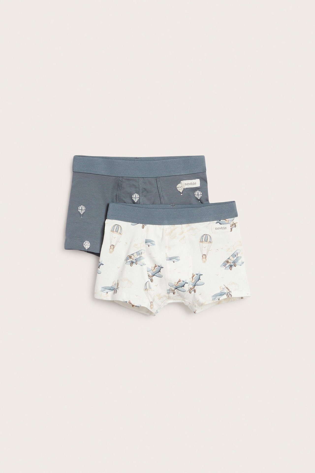 Vorderansicht: Zwei Kinder-Boxershorts. Eine cremefarben mit blauen Flugzeugen, eine petrolfarben mit Heißluftballons.