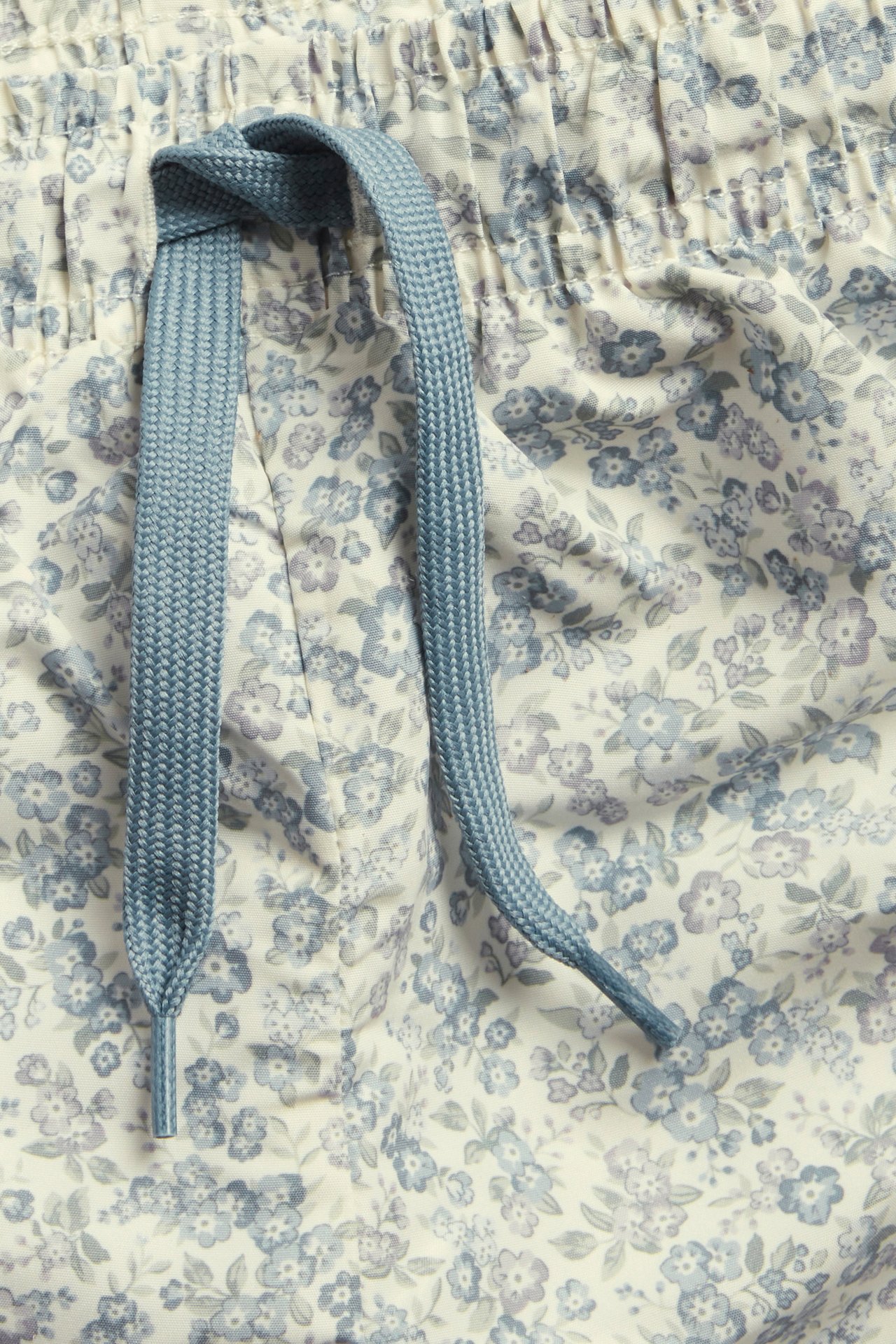 Close-up of beige floral swim shorts with blue flowers, featuring an elastic waistband and blue drawstring.