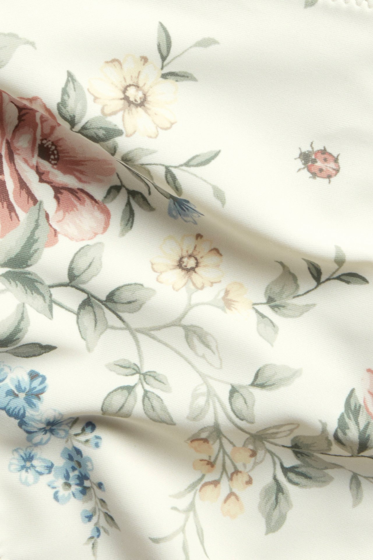 Nahaufnahme von cremefarbenem Bikinihose-Stoff mit Blumenmuster und einem kleinen Marienkäfer.