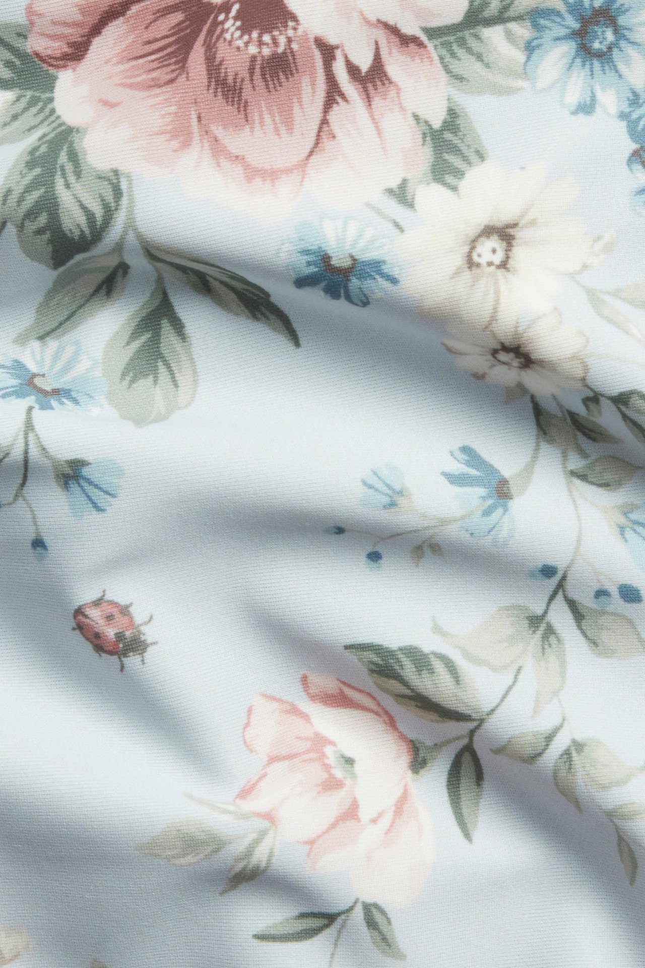 Nahaufnahme des hellblauen Bikinihosenstoffs mit rosa-blauem Blumenmuster und einem Marienkäfer.