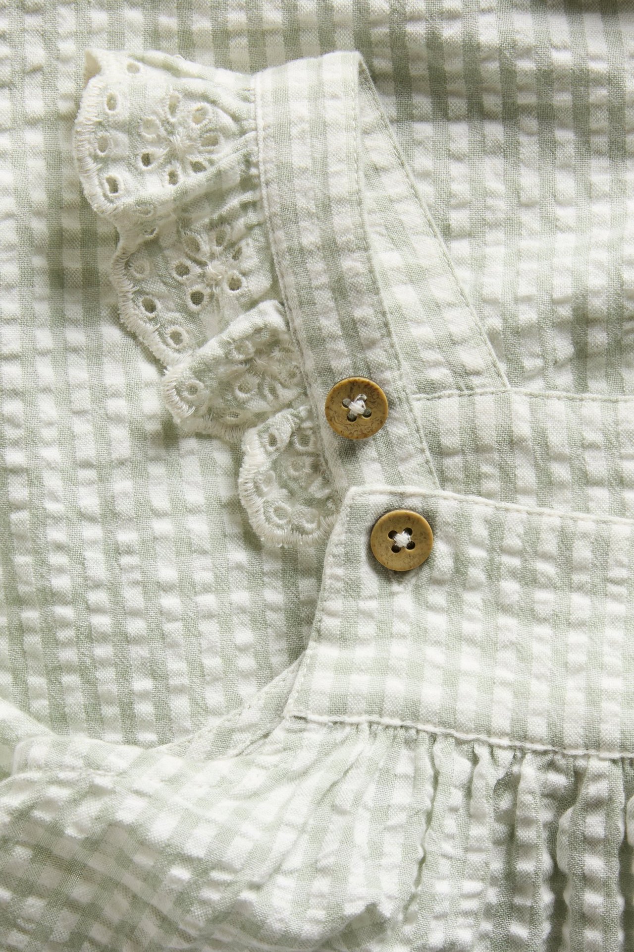Nahaufnahme eines grünen karierten gewebten Babykleides mit bestickten Rüschen und Holzknopfbändern.