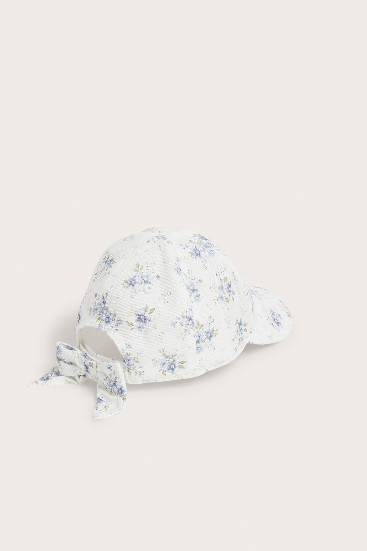 Back view of an off-white kid's cap with blue floral print and a decorative bow.