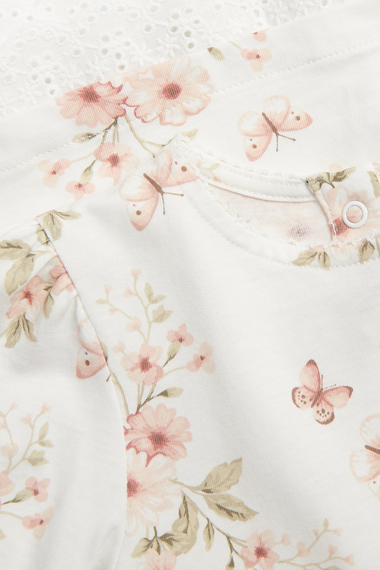 Nahaufnahme: Cremeweißes Baumwollkleid mit Blumen-Schmetterlingsmuster, Rundhalsausschnitt, Rückenknopf und Spitzenbesatz.