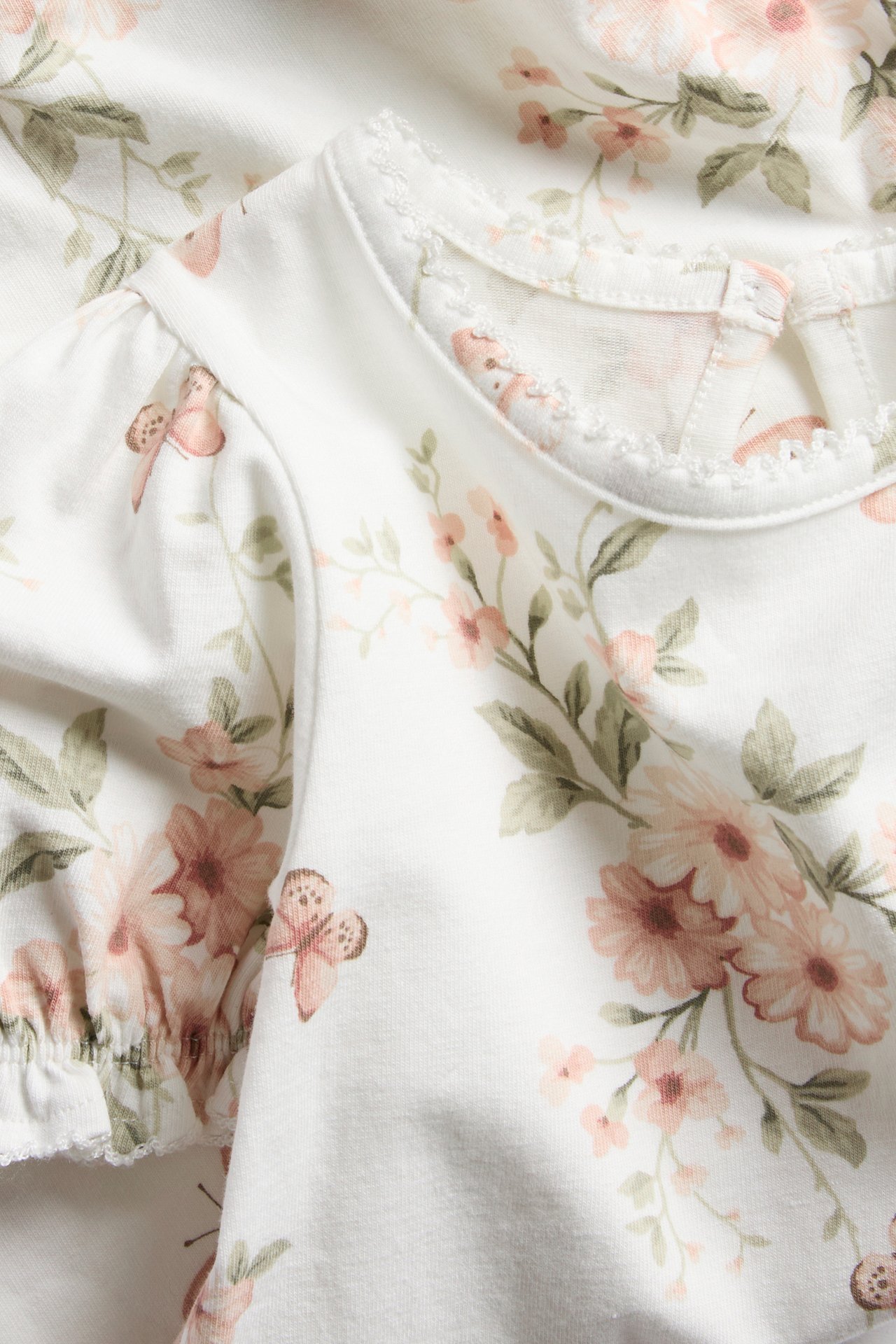 Close-up of an offwhite baby bodysuit with short puff sleeves, lace-trimmed neck, and floral butterfly pattern.
