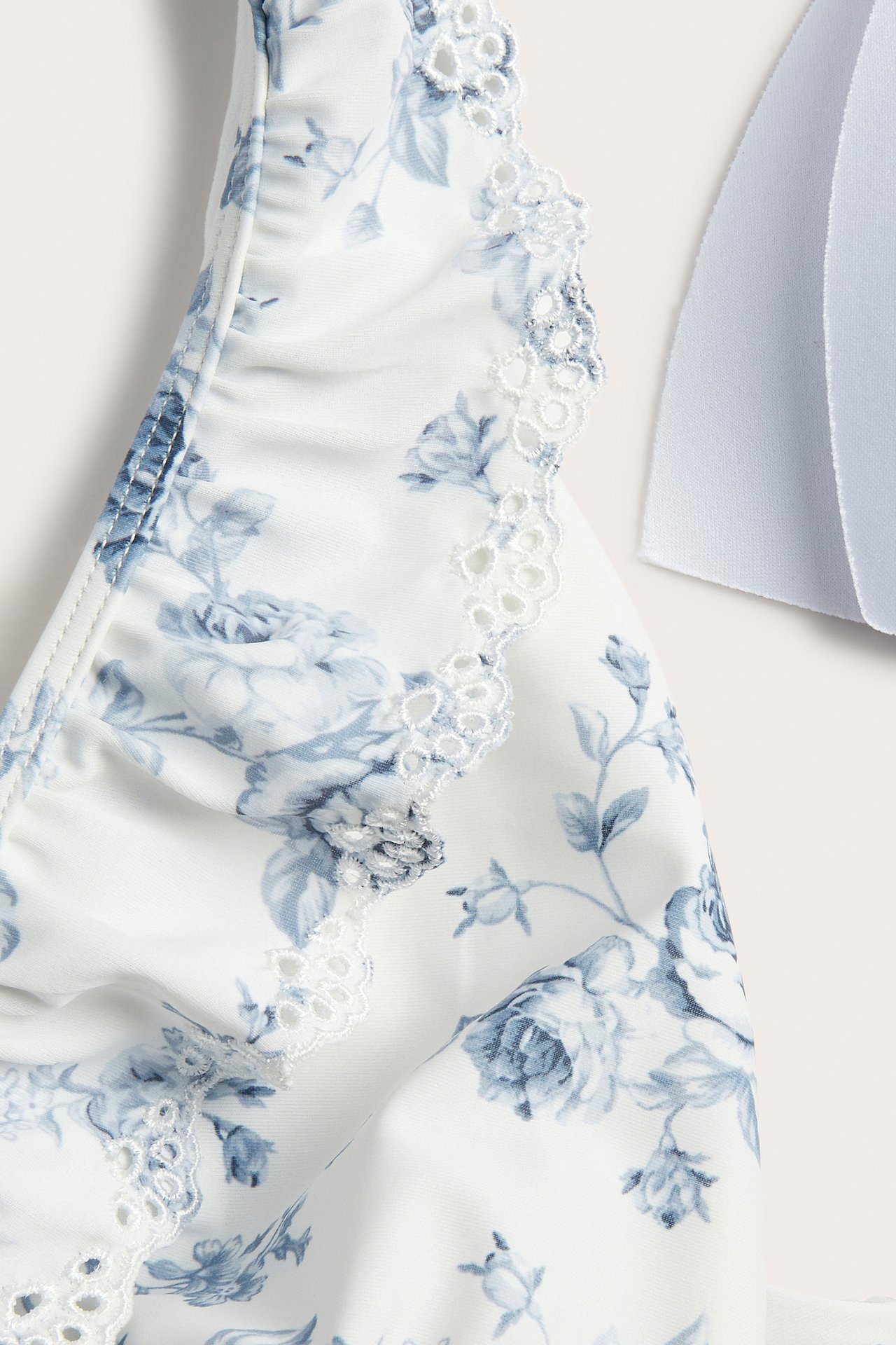 Close-up of an off-white floral swimsuit with blue pattern and white embroidered ruffle on shoulder.