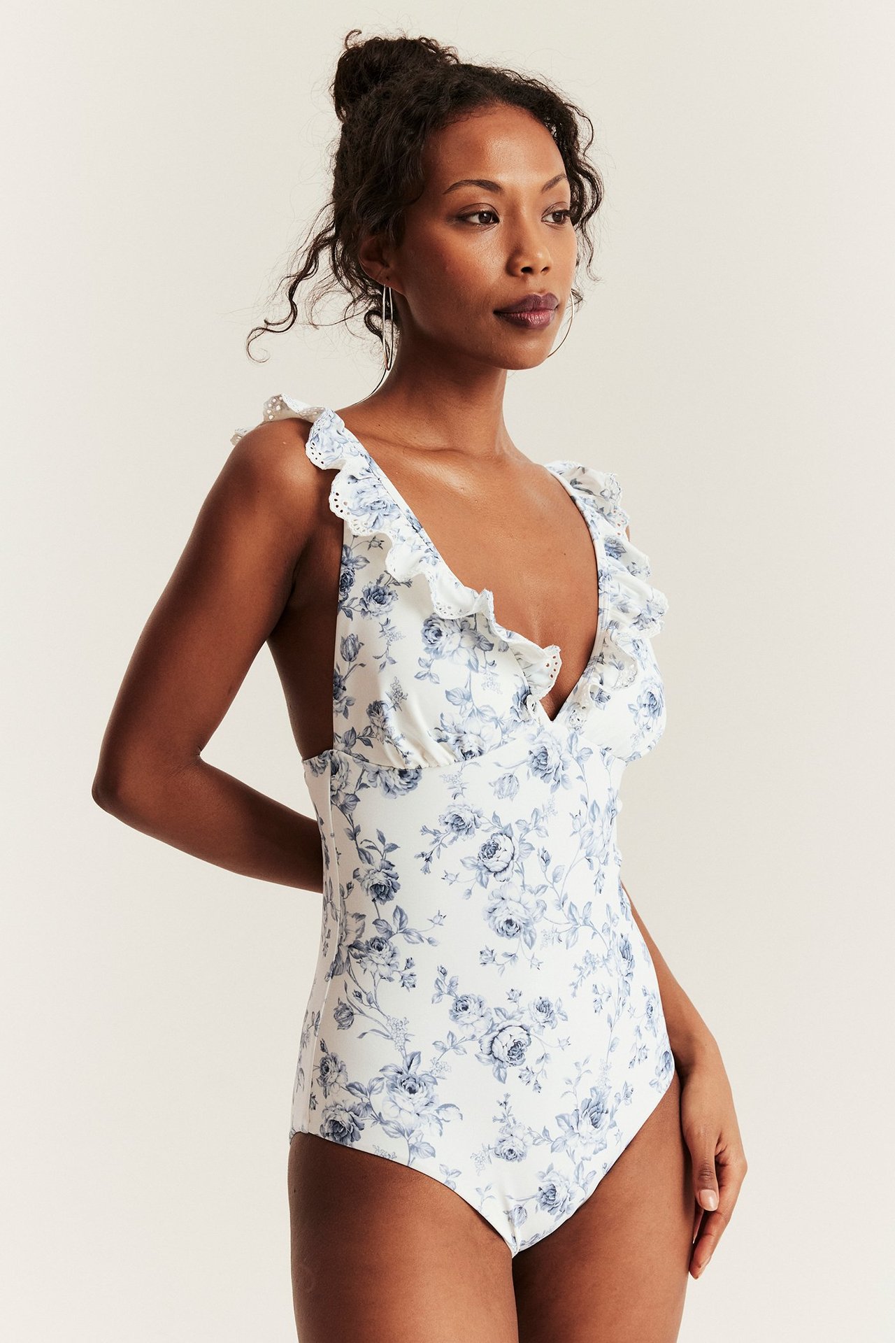 Front view of woman wearing an off-white floral V-neck swimsuit with ruffled, embroidered shoulder straps.