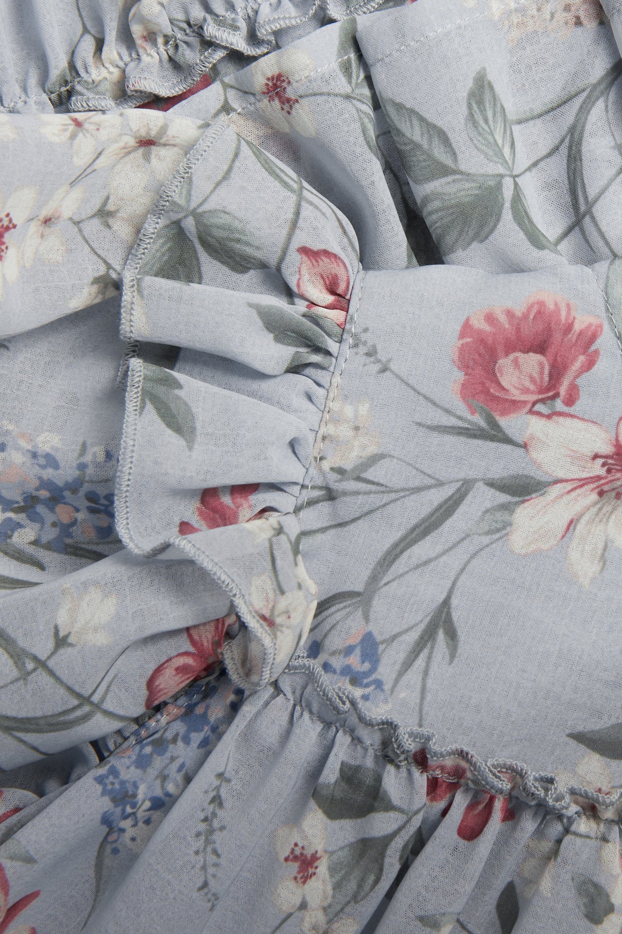Close-up of a light blue chiffon dress with a floral pattern and gathered ruffles.
