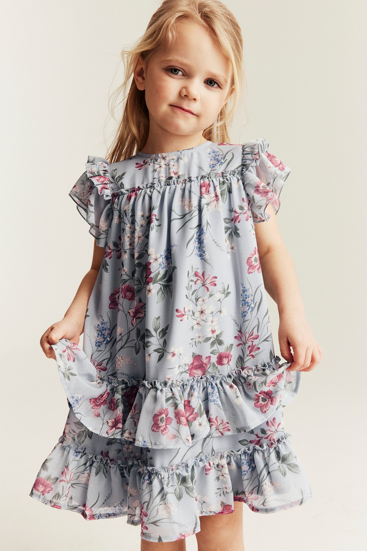 Front view: Kid wears a light blue floral chiffon dress, ruffled sleeves, and tiered skirt.