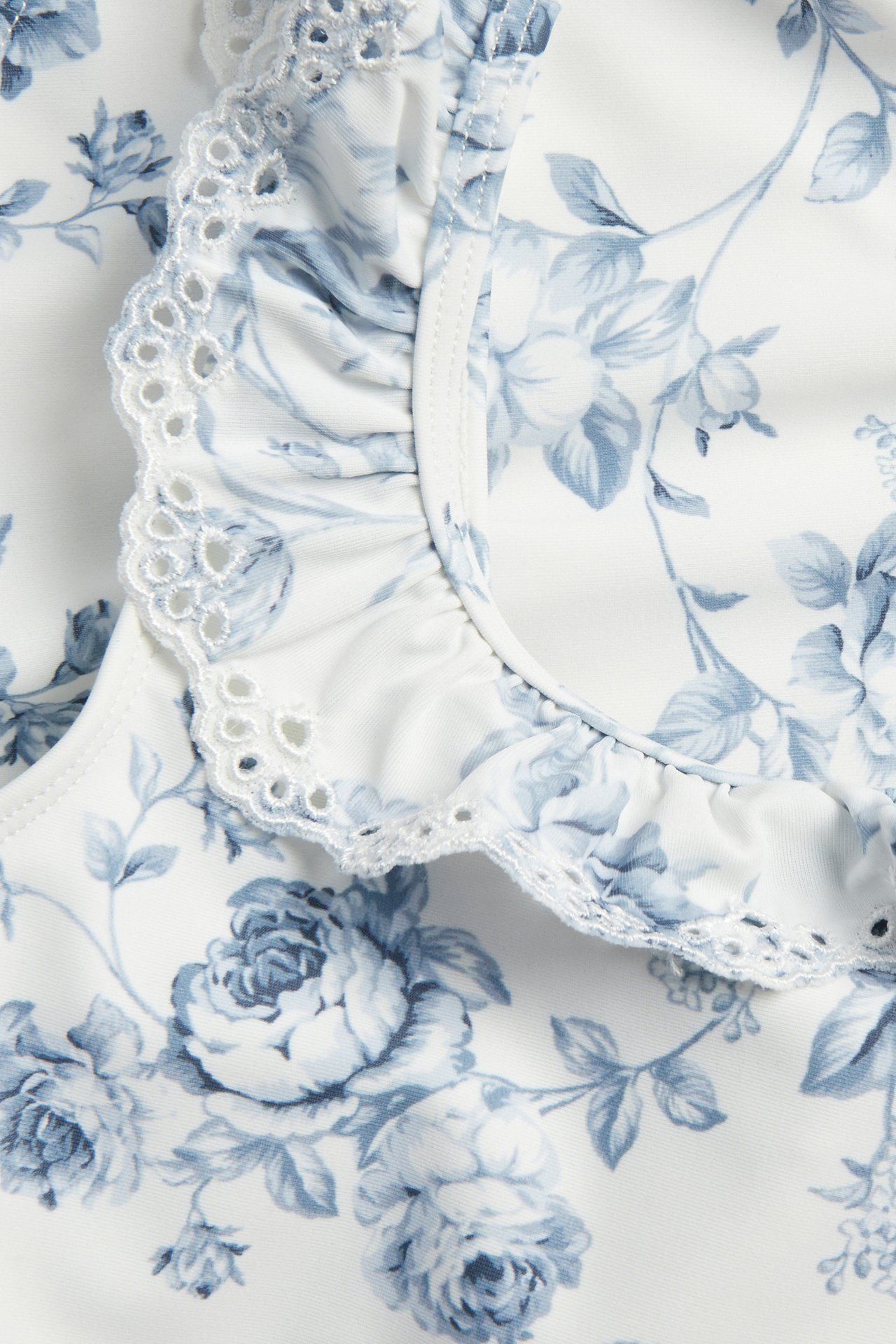 Close-up of an off-white floral swimsuit with blue flowers and an embroidered ruffle.