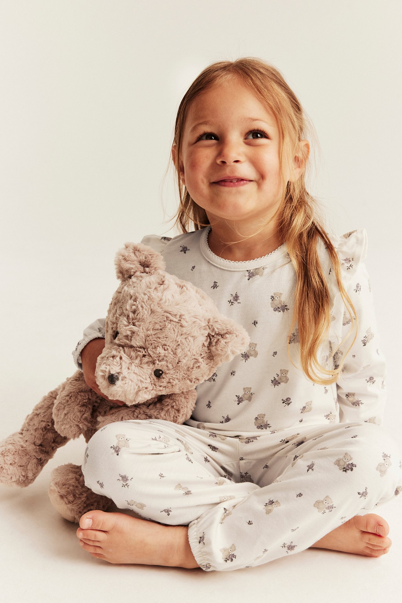 Vorderansicht Kinder-Pyjama, weiß mit Bärenmuster, Langarm-Oberteil, Hose, hält braunen Teddybär.