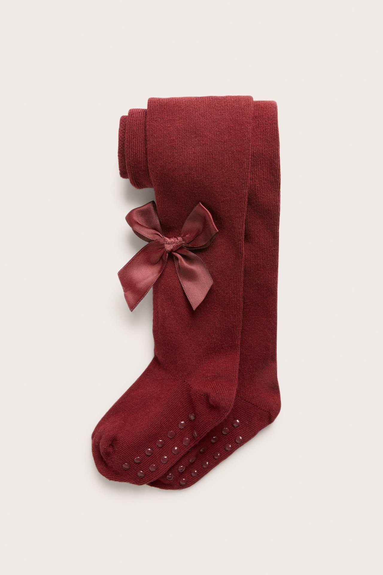 Vorderansicht dunkelroter Strick-Babystrumpfhosen mit Satinschleife und Anti-Rutsch-Noppen an der Sohle.