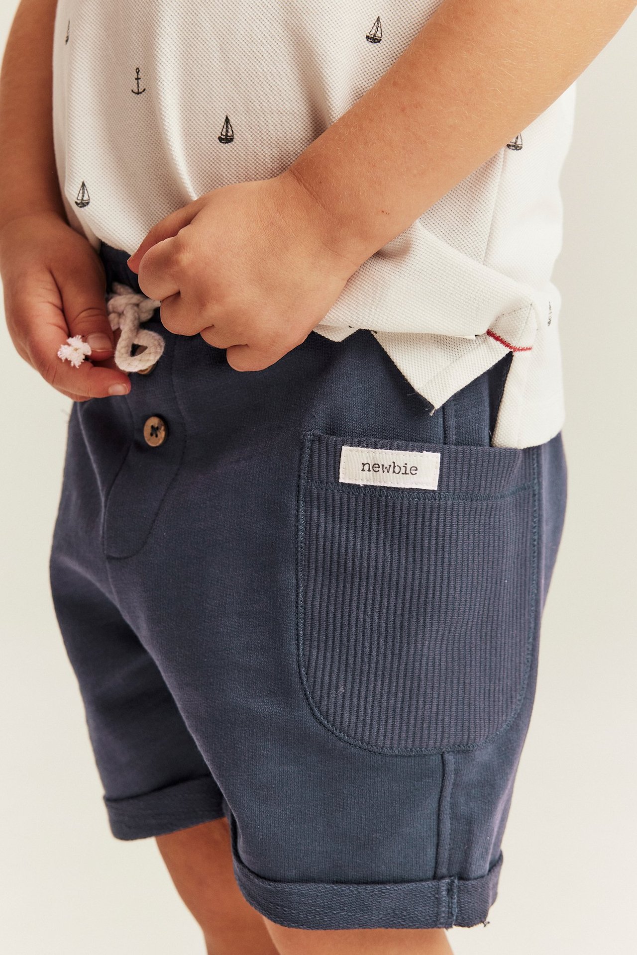 Nahaufnahme Kind in dunkelblauen Shorts mit Krempelbündchen und weißem gemusterten Poloshirt.