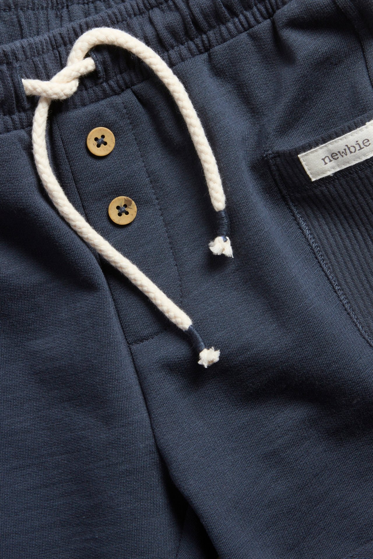 Nahaufnahme dunkelblauer Slub-Jersey-Shorts mit elastischem Bund, weißem Kordelzug, dekorativen Knöpfen und Ripptasche.