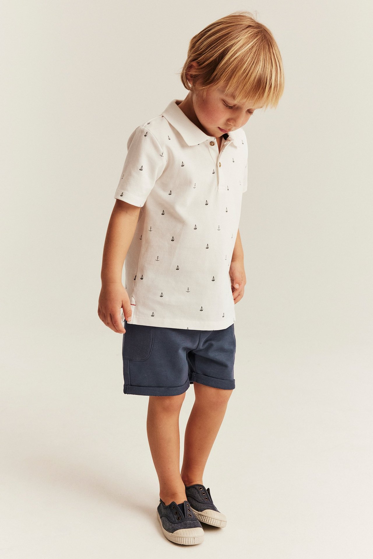 Side view of a kid wearing dark blue slub shorts with ribbed pockets and a white anchor polo shirt.