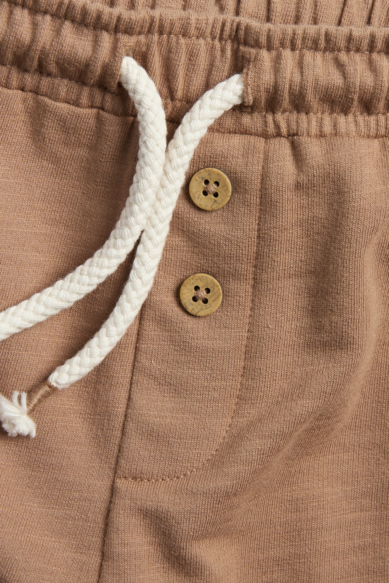 Close-up of brown slub jersey shorts with a white drawstring and decorative brown buttons on the front.