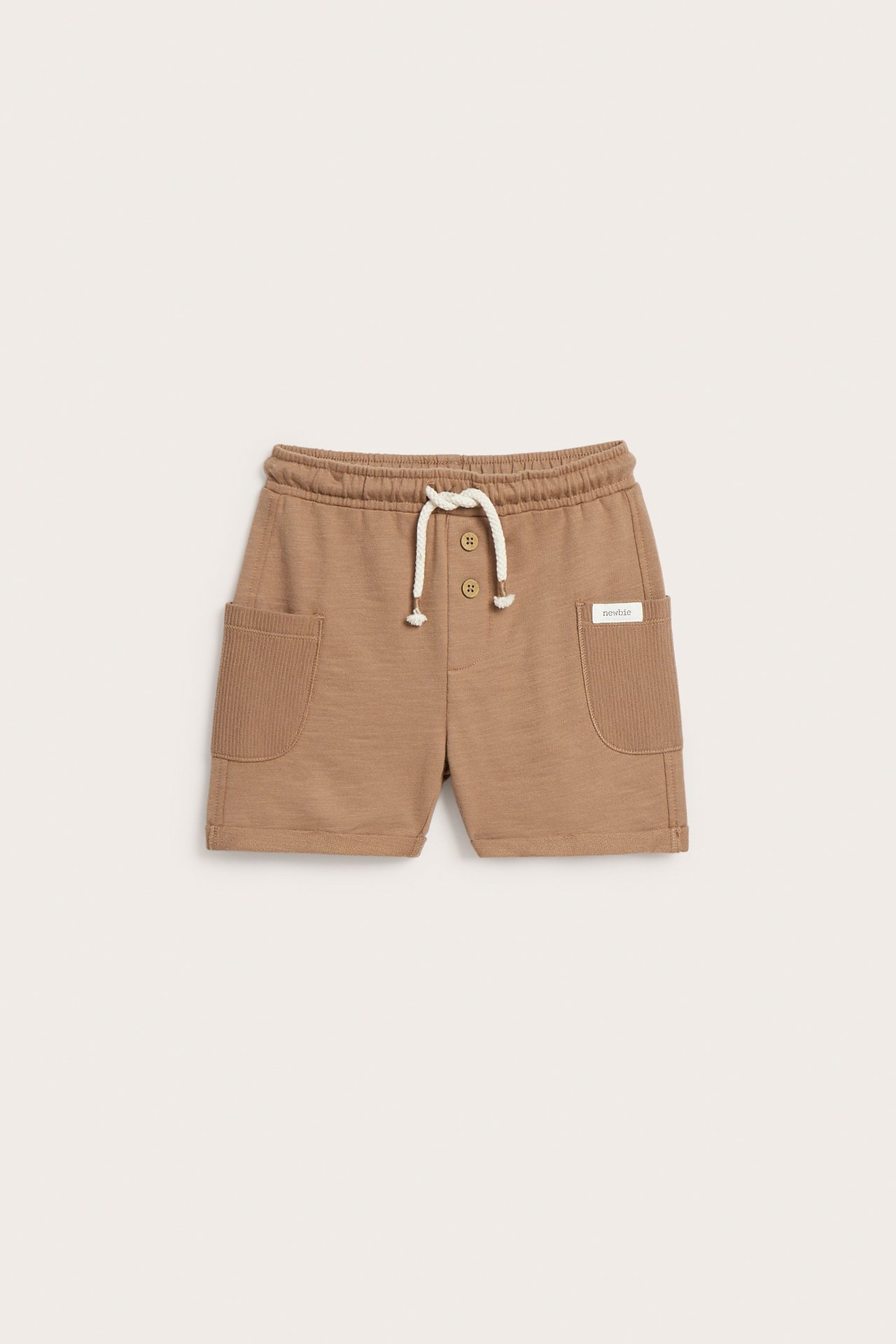 Front view: brown kid's cotton slub jersey shorts with ribbed side pockets, decorative buttons, and white drawstring.