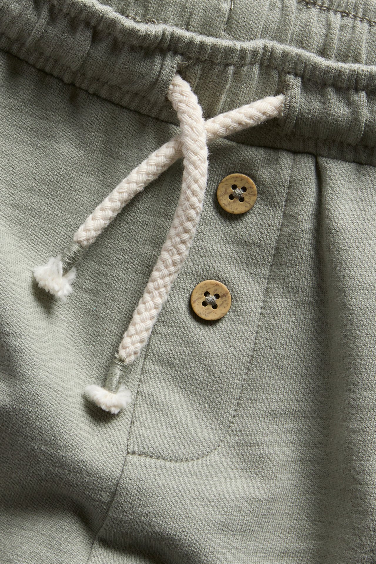 Nahaufnahme dunkelgrüner Slub-Jersey-Shorts mit Gummizug, weißem Kordelzug und zwei Holzknöpfen.