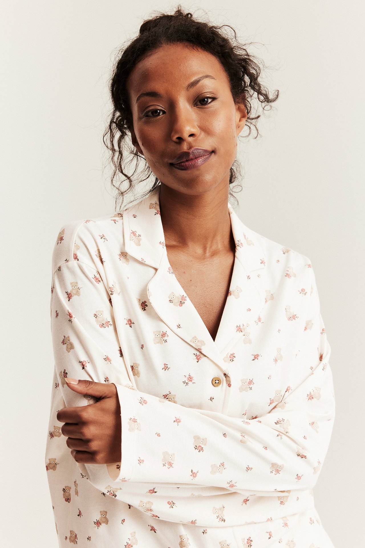 Woman wears off-white long-sleeved cotton pajama top with teddy bear pattern and front buttons.