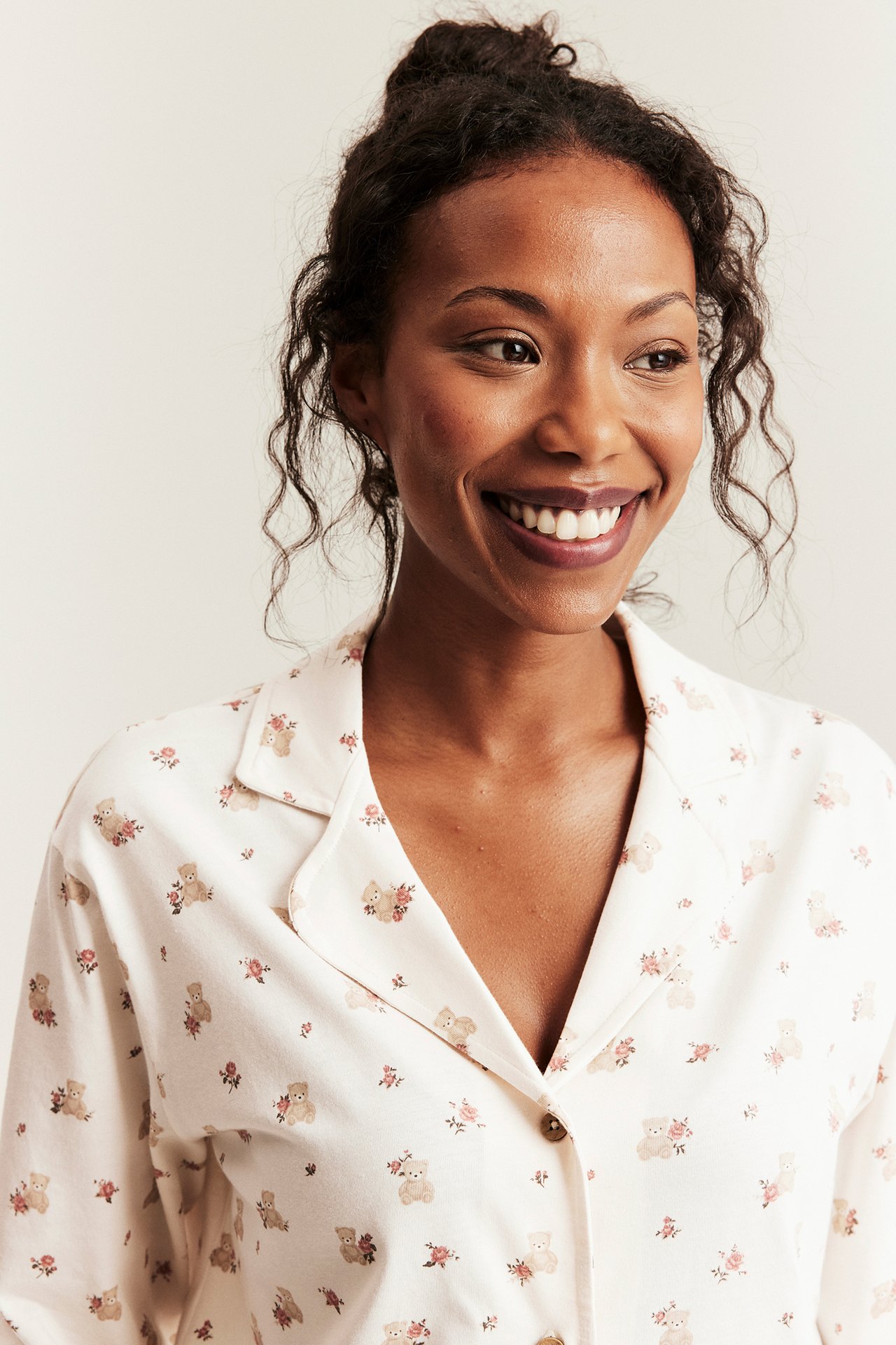 Close-up of woman wearing off-white cotton pyjama top with teddy bear, floral print, and front buttons.