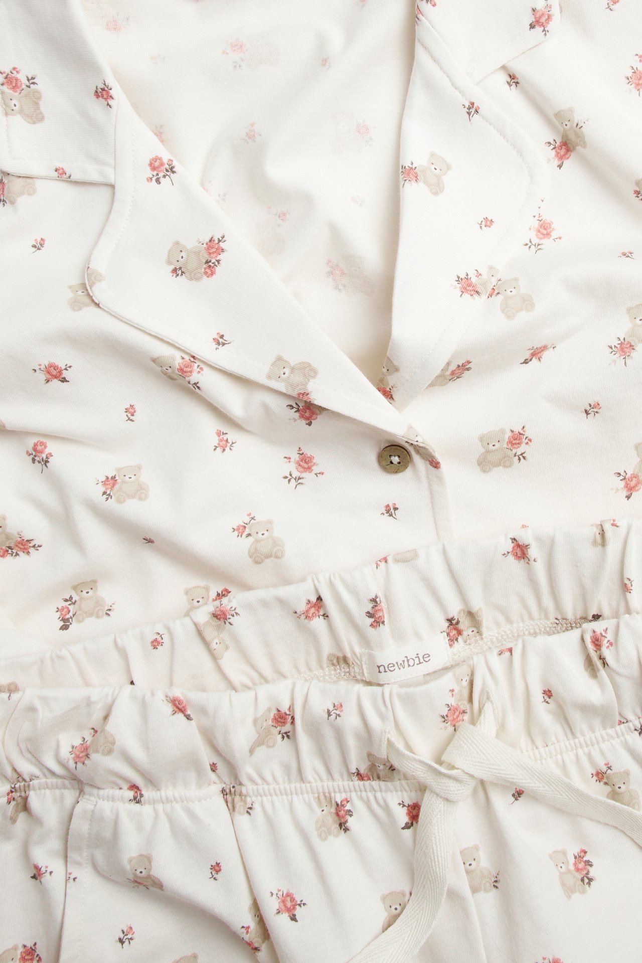 Close-up of off-white cotton pyjama set with floral and teddy bear pattern, featuring a buttoned top and drawstring shorts.