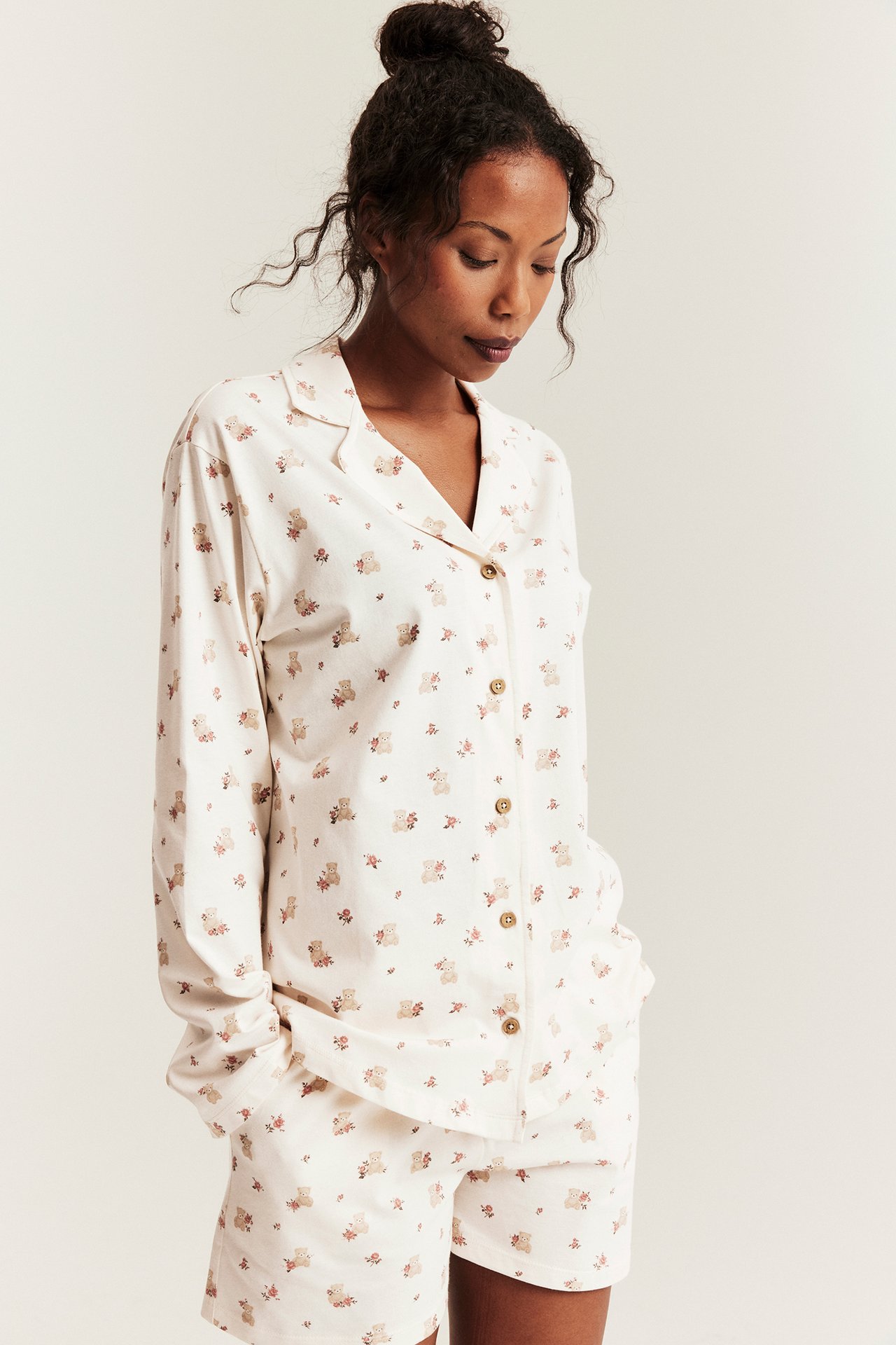 Front view: Woman in off-white cotton pajama set with bear and floral print top and matching shorts.