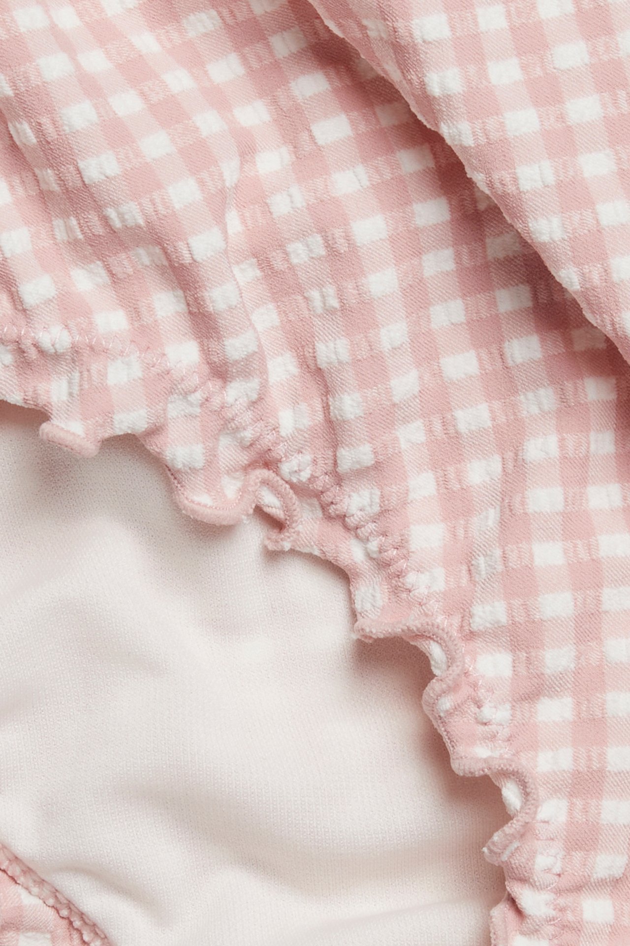 Close-up of a pink and white checkered bikini bottom with a ruffled edge and light pink lining.