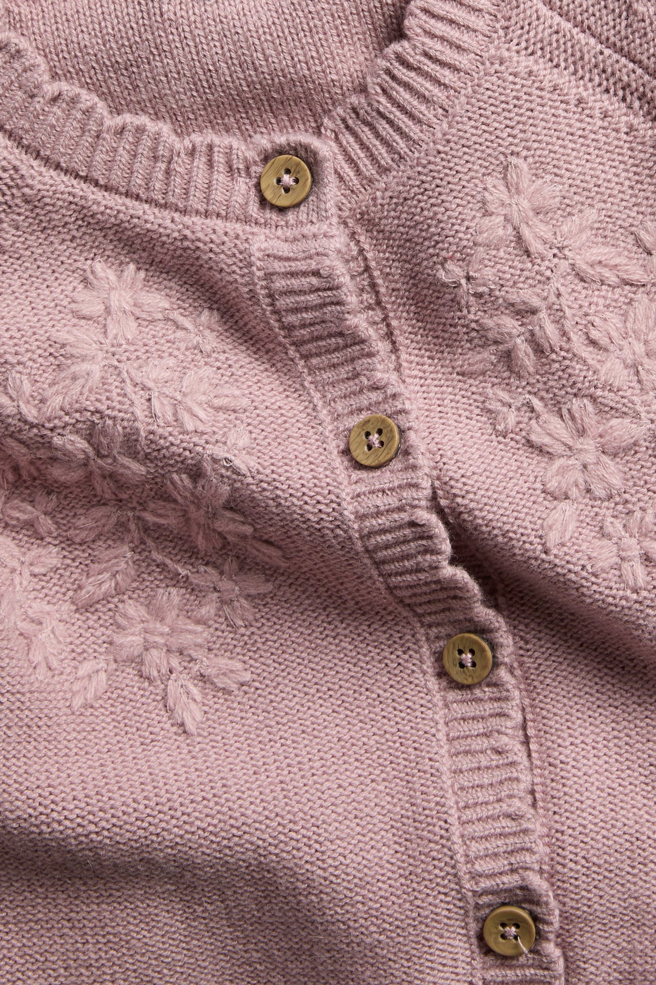 Nahaufnahme einer rosa Strickjacke mit bestickten Blumendetails und Holzknöpfen.
