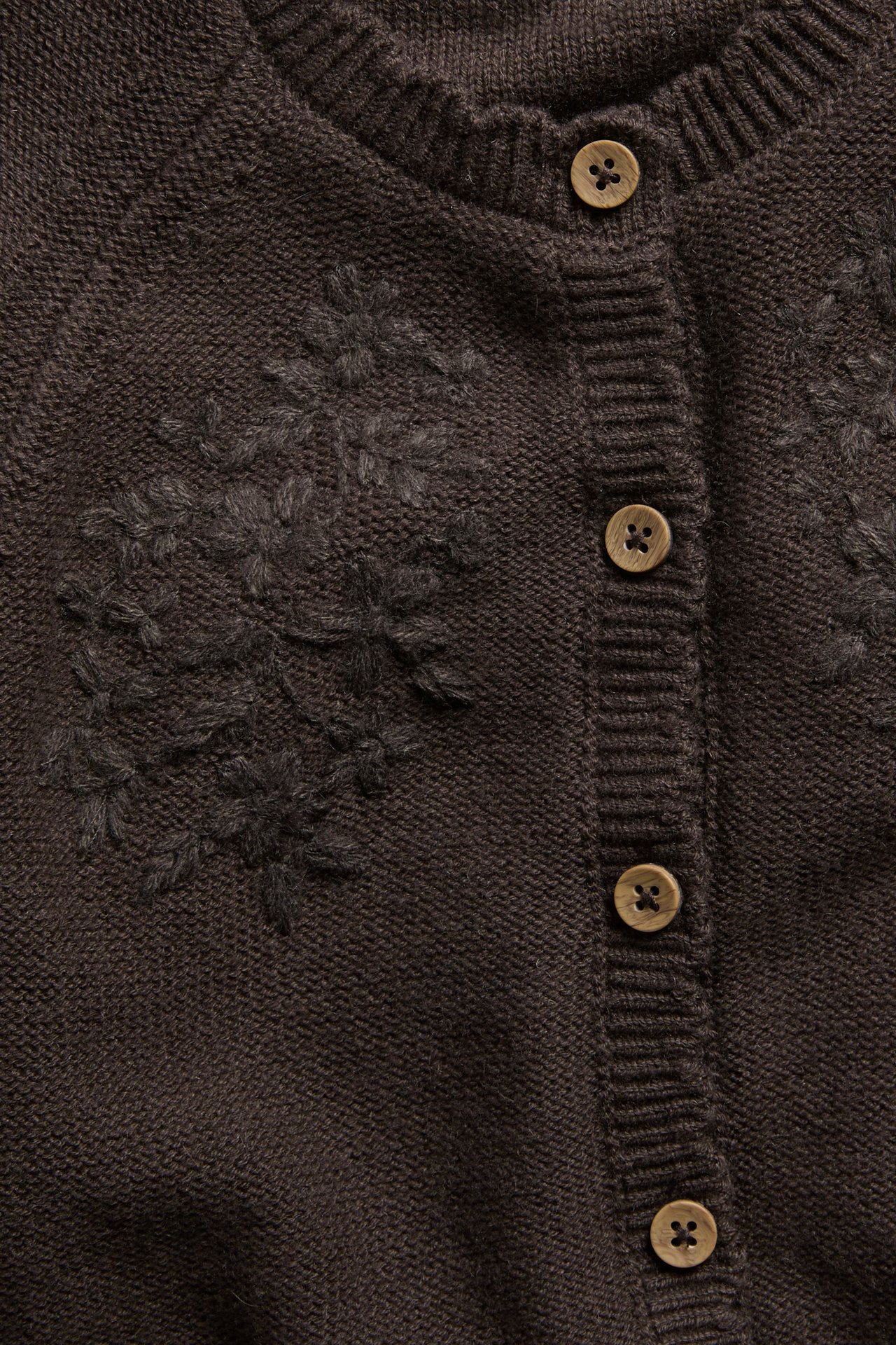 Close-up of a dark brown knitted cardigan with floral embroidery and wooden button fastenings.