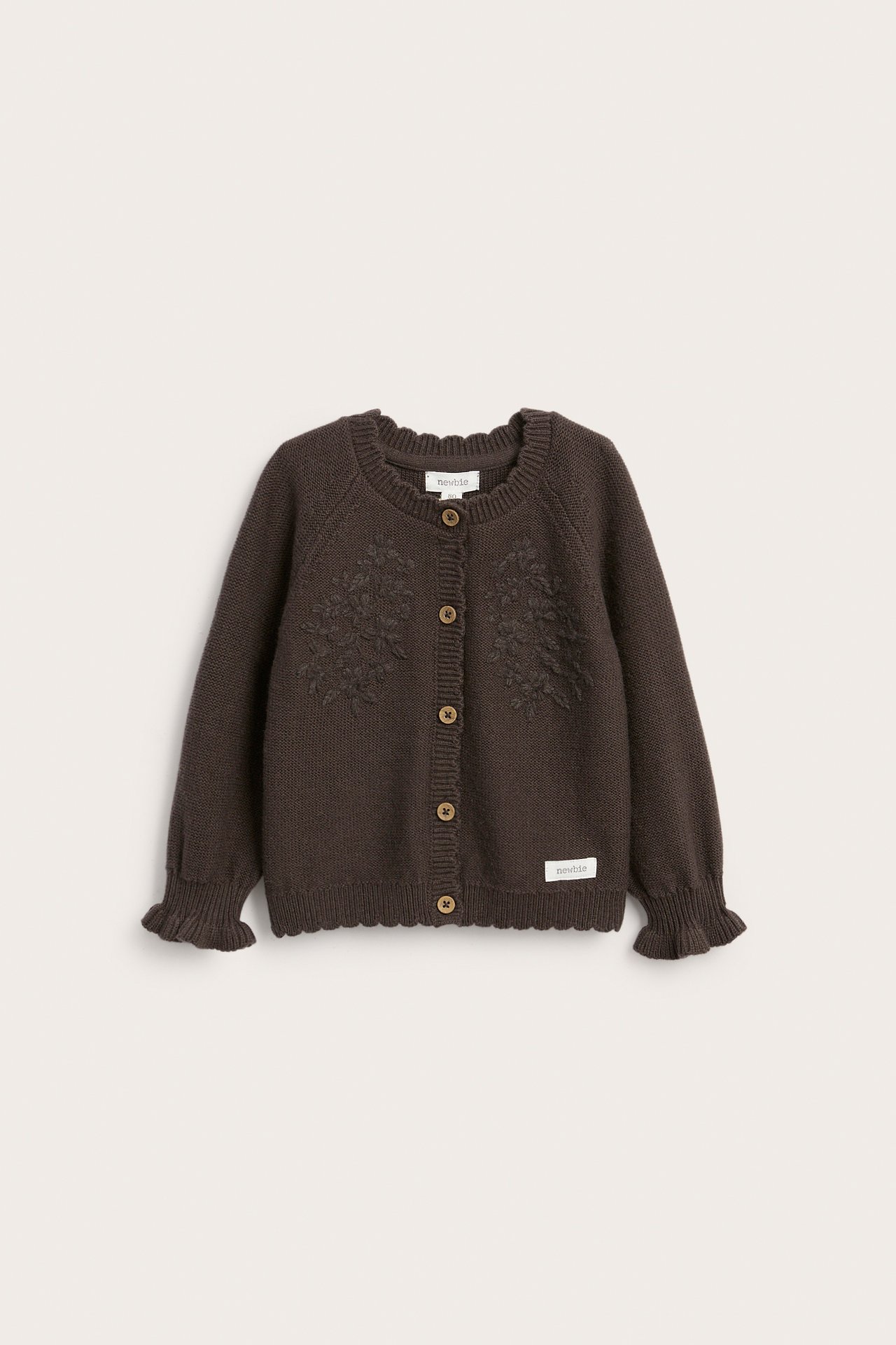 Vorderansicht einer dunkelbraunen Strickjacke für Kinder mit Rüschenbündchen, Muschelsaum und Stickereien.