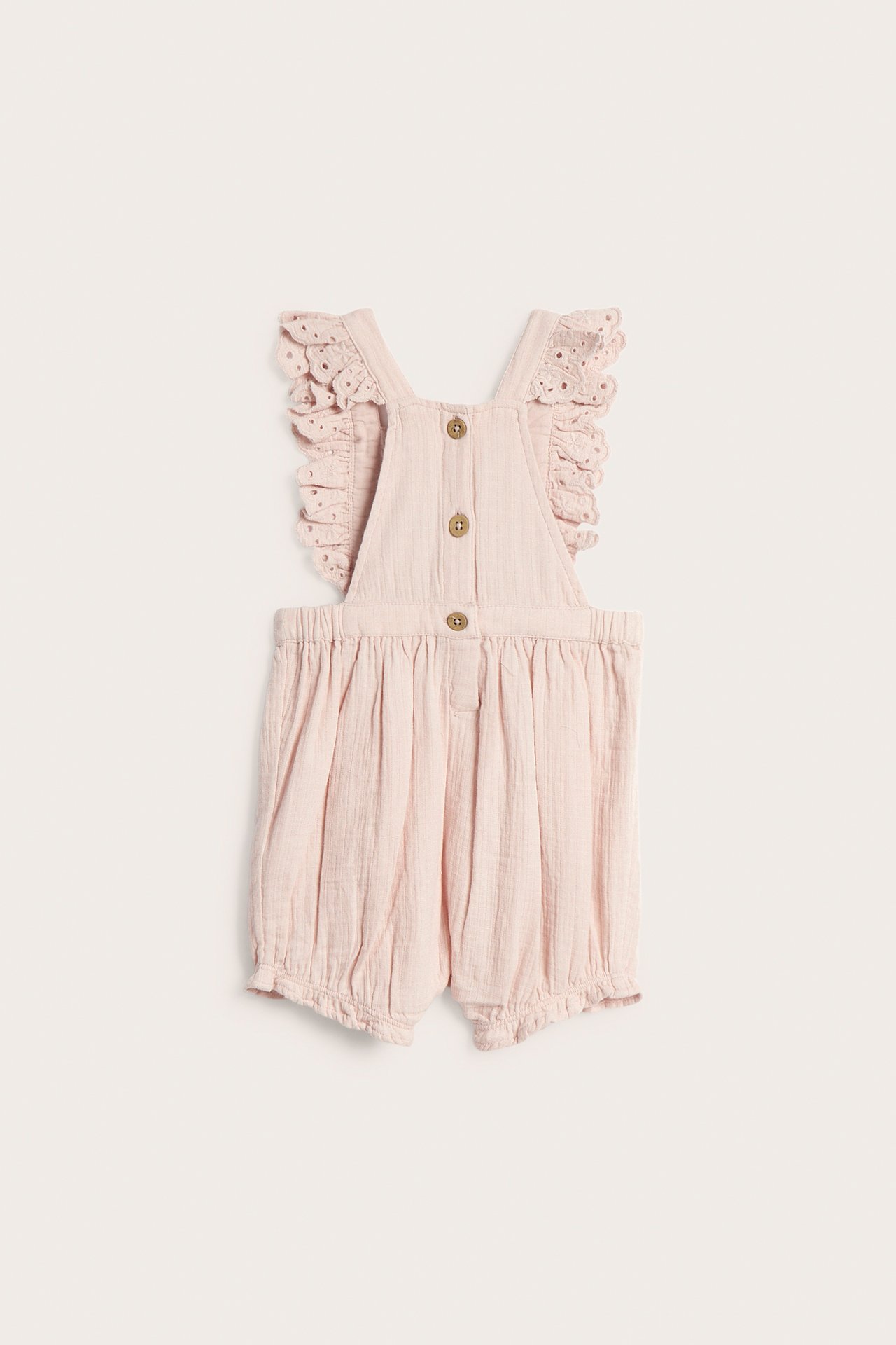 Vorderansicht: Baby-Latzshorts aus hellrosa Baumwolle mit Spitzenrüschen an den Trägern und Holzknöpfen.