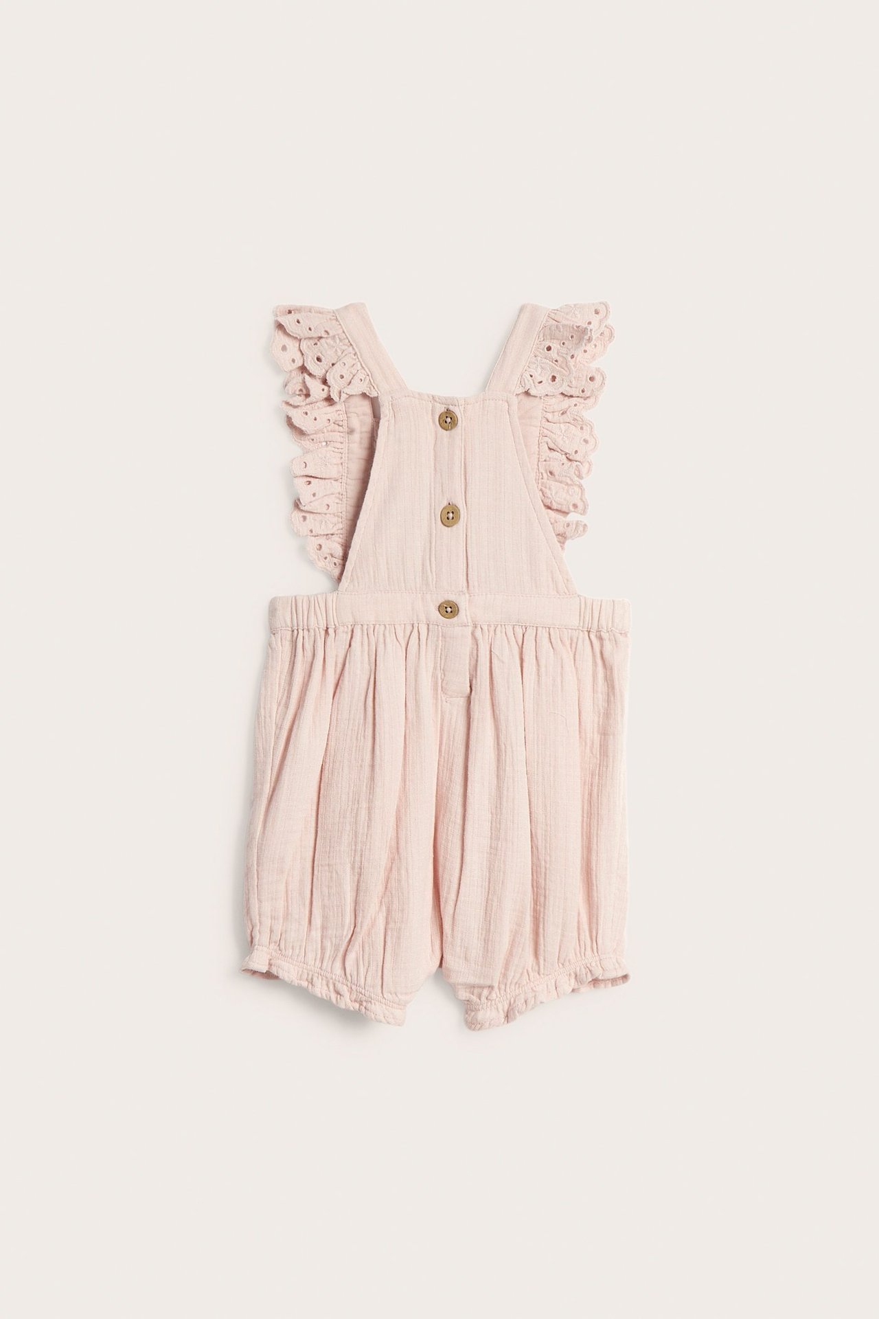 Vorderansicht: Baby-Latzshorts aus hellrosa Baumwolle mit Spitzenrüschen an den Trägern und Holzknöpfen.