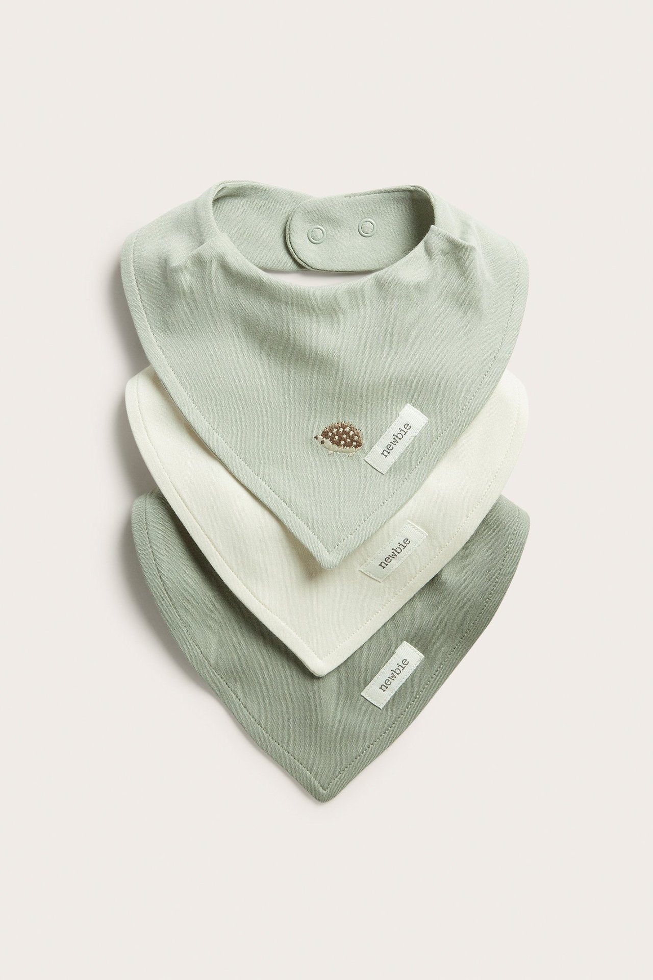 Vorderansicht: Drei weiche Baby-Baumwoll-Lätzchen. Hellgrün mit Igel-Stickerei, cremefarben und dunkelgrün. Druckknöpfe.