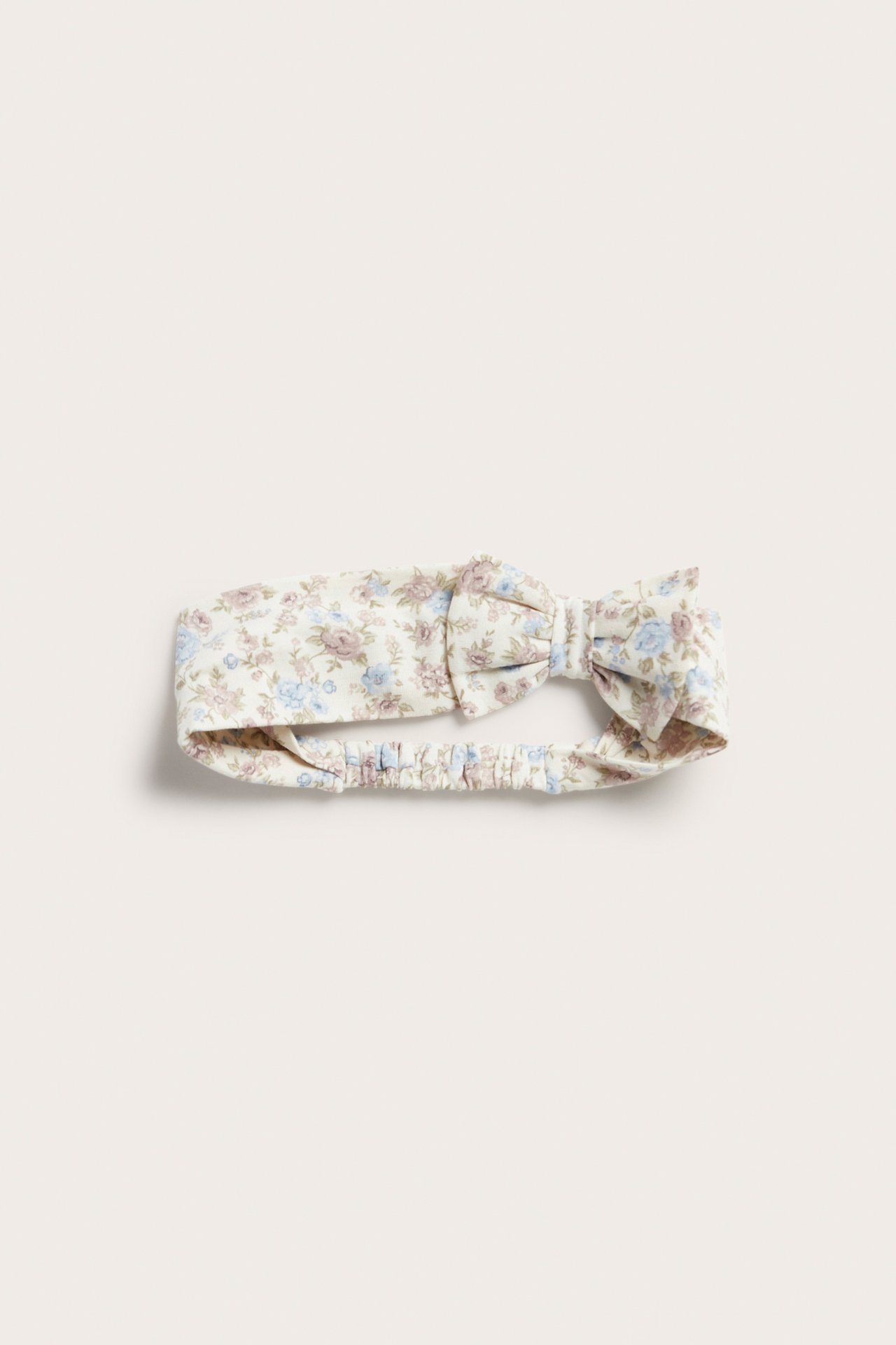 Front view of an offwhite small floral cotton jersey headband with a bow and elastic at the back.