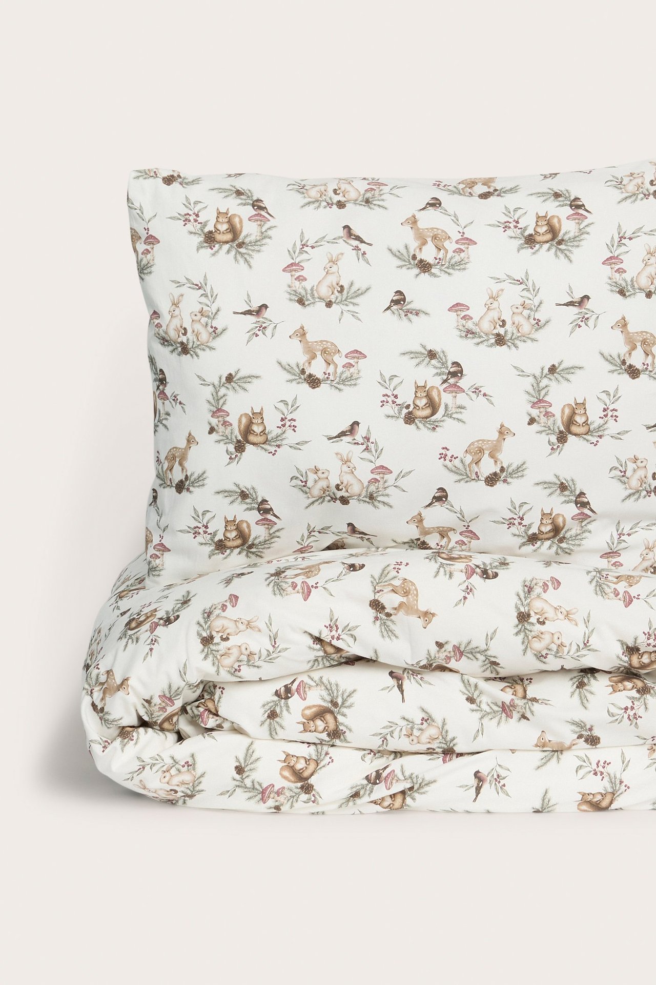 Nahaufnahme eines cremeweißen Baumwoll-Bettwäschesets mit detailliertem weihnachtlichem Waldtiermuster.