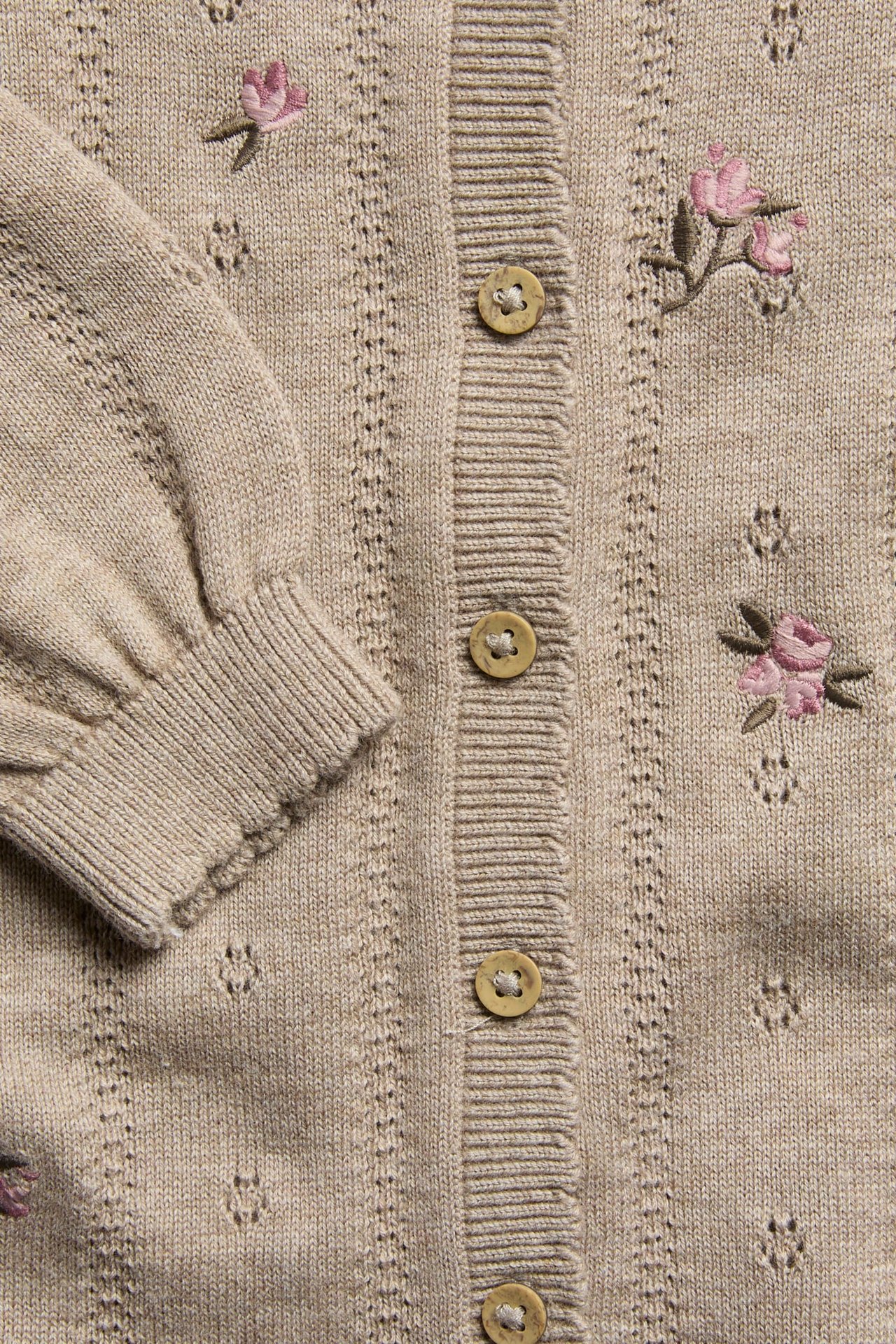 Nahaufnahme einer beigen Strickjacke mit gestickten rosa Rosen und Knöpfen vorne.