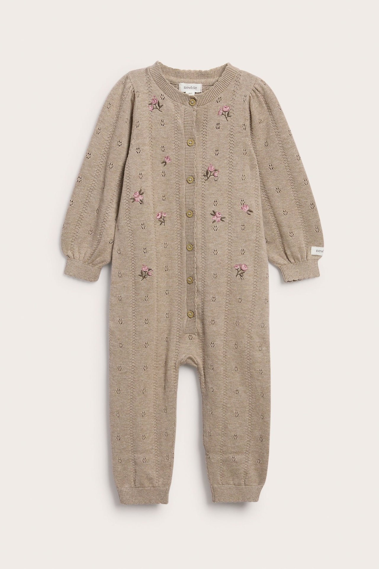 Vorderansicht eines beigefarbenen gestrickten Baby-Overalls mit rosa Stickblumen und Knöpfen vorne.