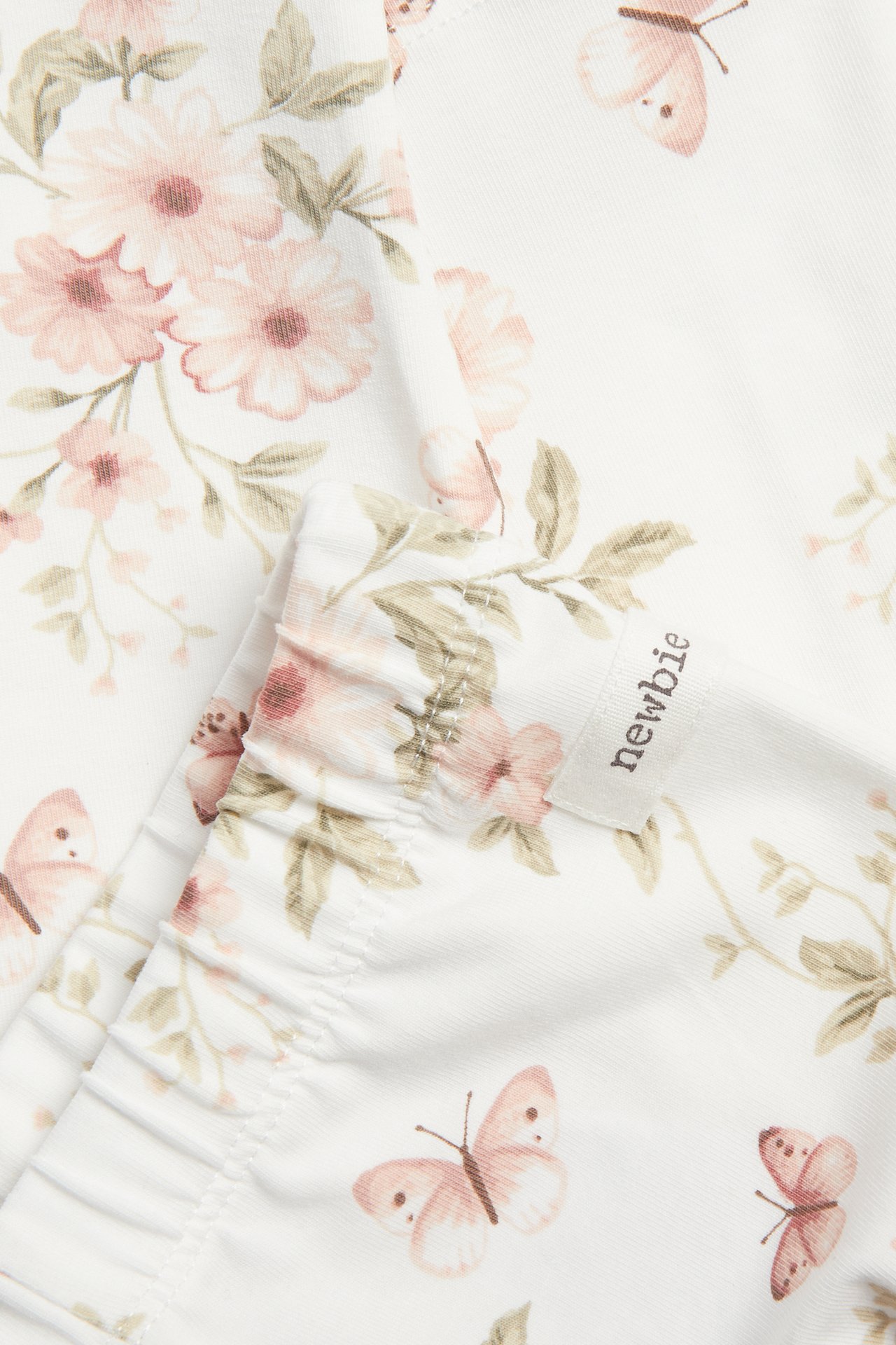 Close-up of off-white jersey leggings with pink floral and butterfly pattern, elasticated edge.