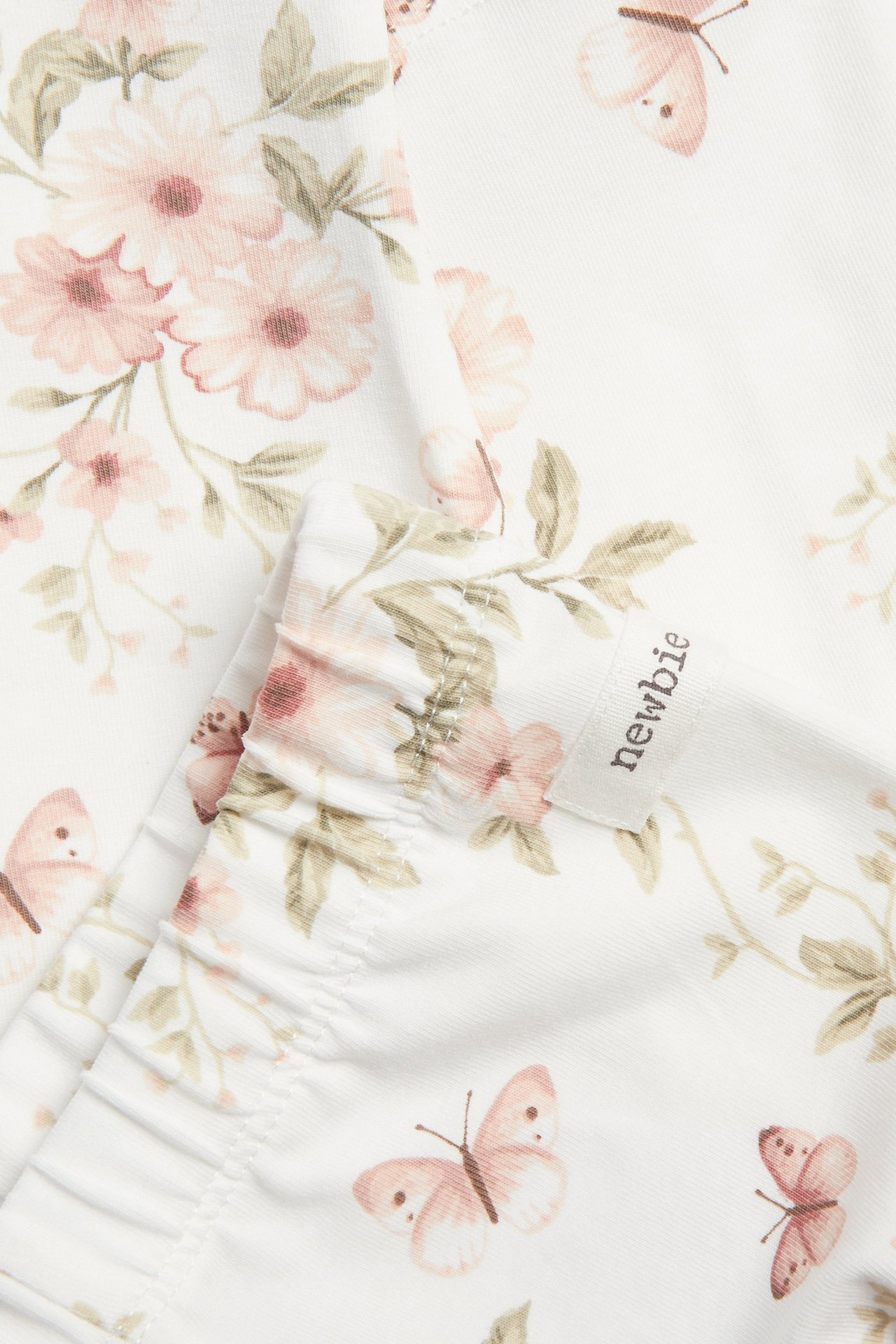 Nahaufnahme von off-white Jersey-Leggings mit rosa Blumen- und Schmetterlingsmuster, elastischer Bund.