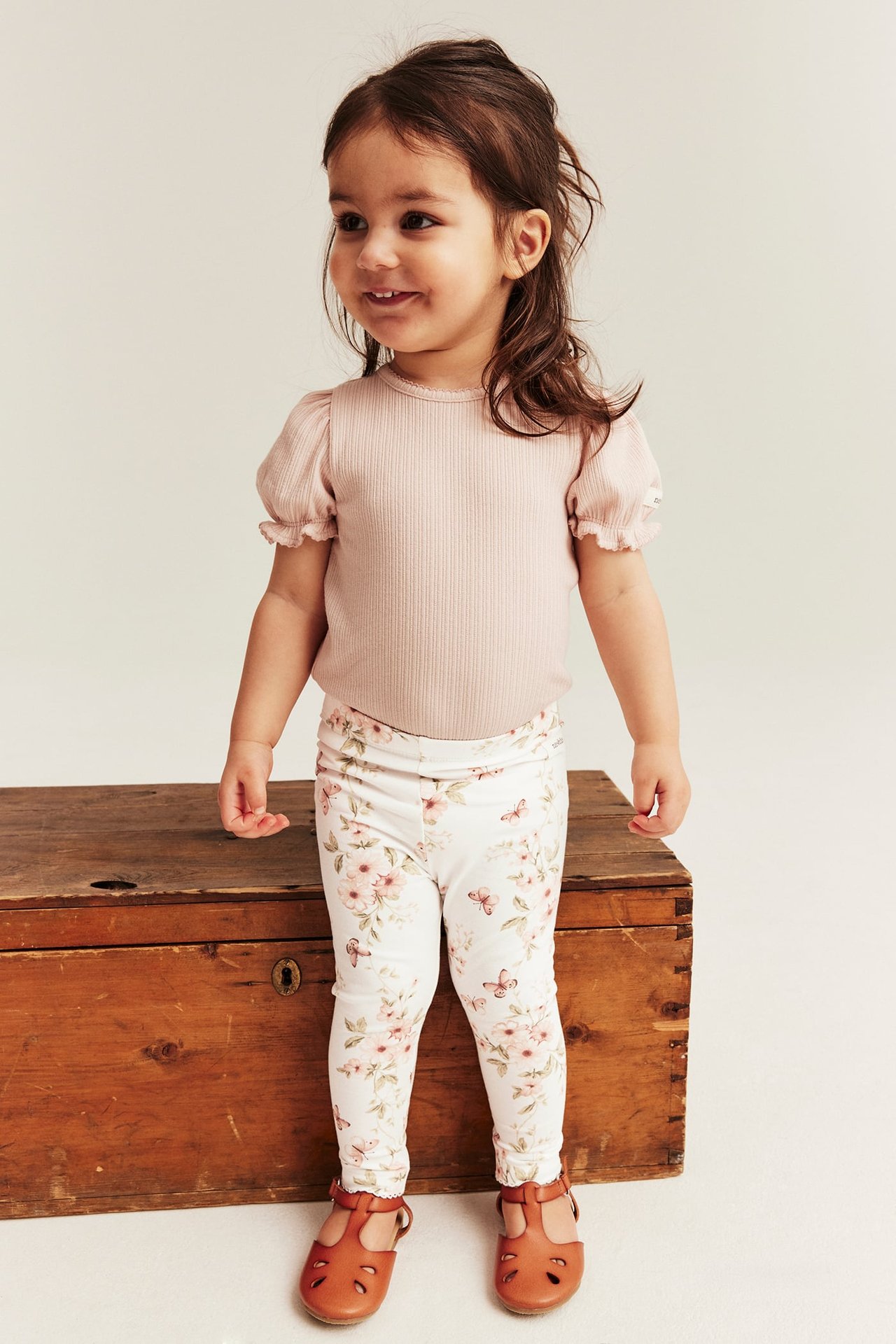 Front view of a kid in off-white floral leggings, light pink ribbed top, and brown shoes.