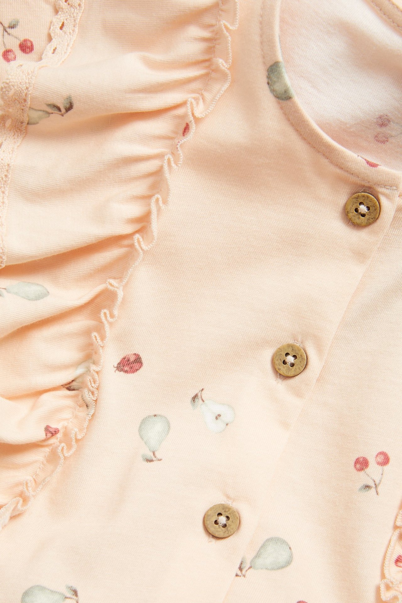 Close-up of an orange patterned baby jersey jumpsuit with ruffles, lace trim, and wooden buttons.