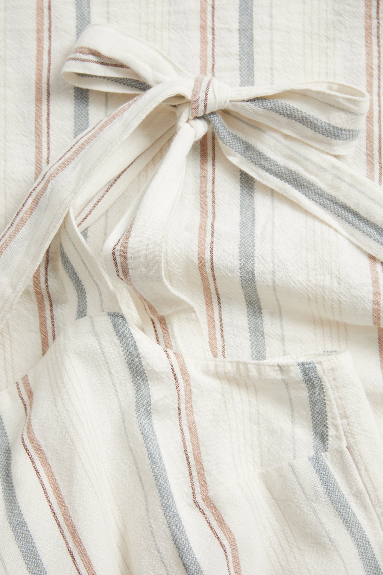 Nahaufnahme eines gestreiften Baumwollkleides in Offwhite mit rotbraunen und blaugrauen Streifen, mit Bindeschulterträger.