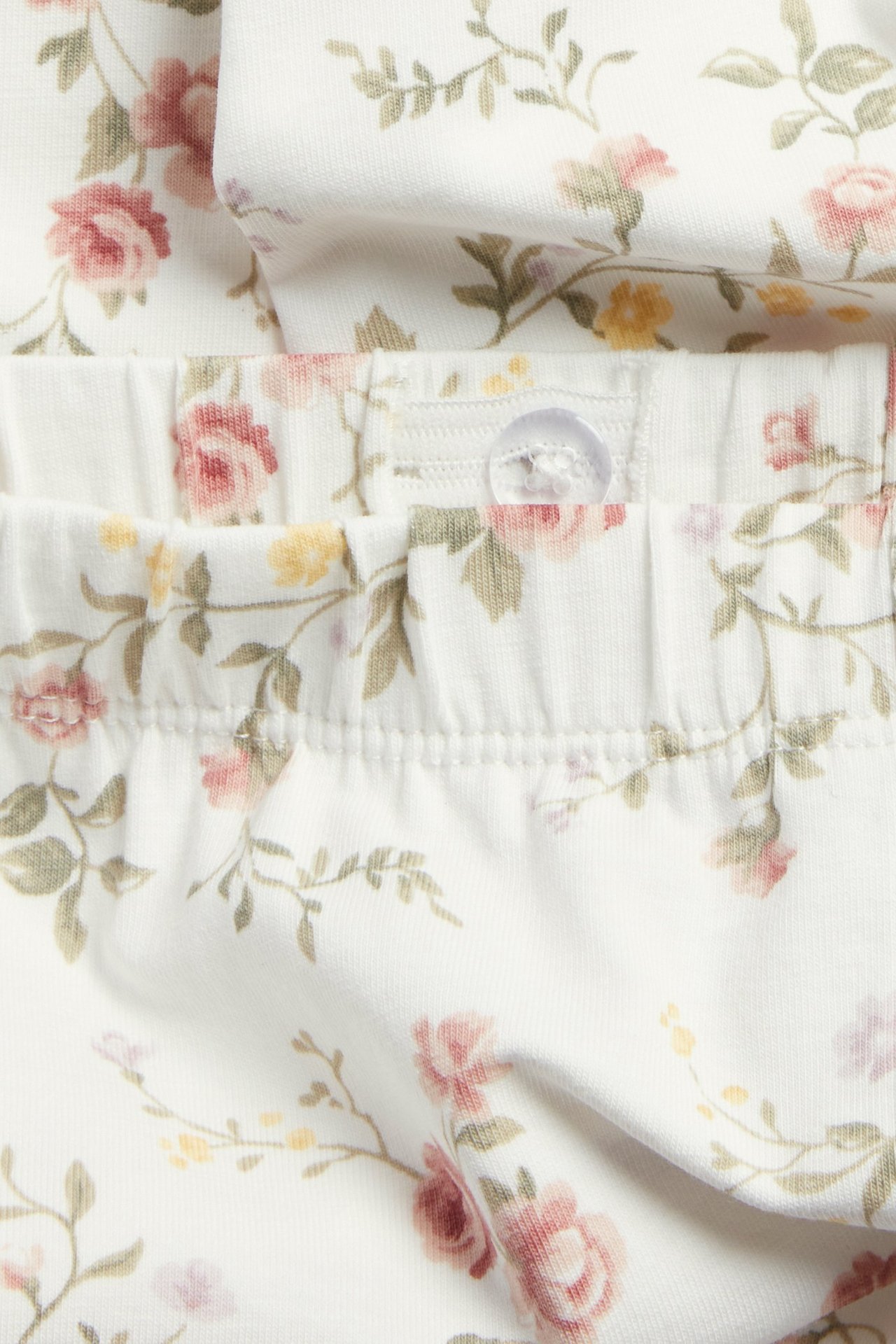 Nahaufnahme von cremeweißen geblümten Leggings mit Gummibund und transparentem Knopf.