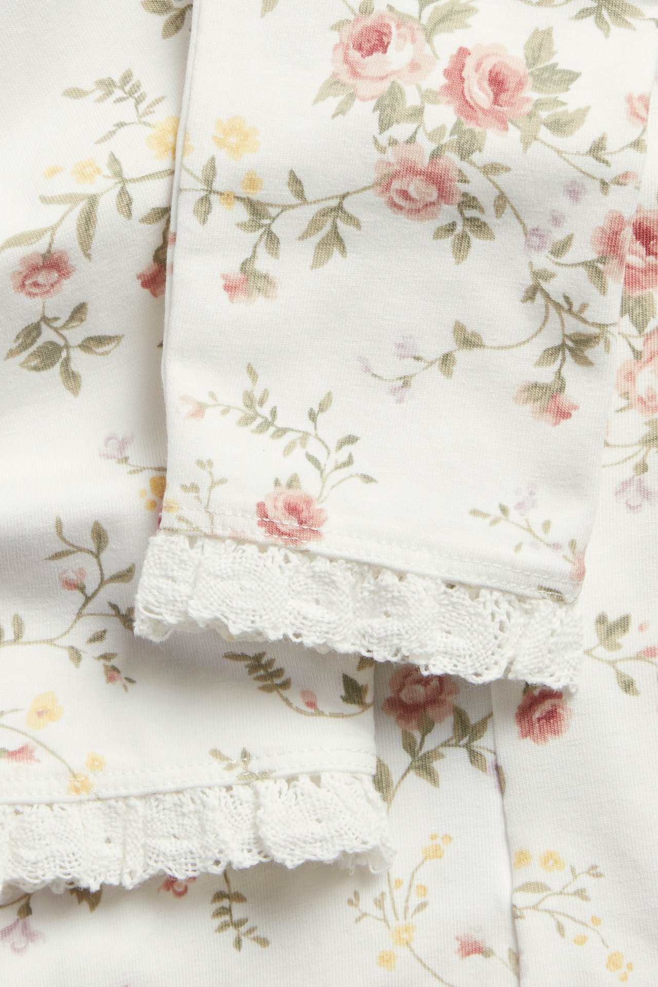 Nahaufnahme von cremeweißen floralen Leggings mit Spitzenrüsche am Beinabschluss.