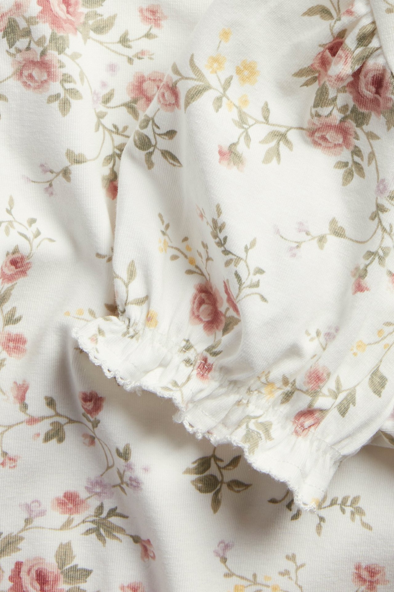 Close-up of an off-white floral jersey top with short puff sleeves and ruffled picot stitch cuffs.