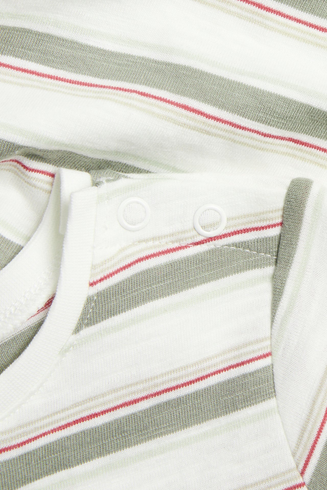 Nahaufnahme eines cremefarbenen Baby-Bodys mit grünen, roten Streifen und weißen Druckknöpfen an der Schulter.