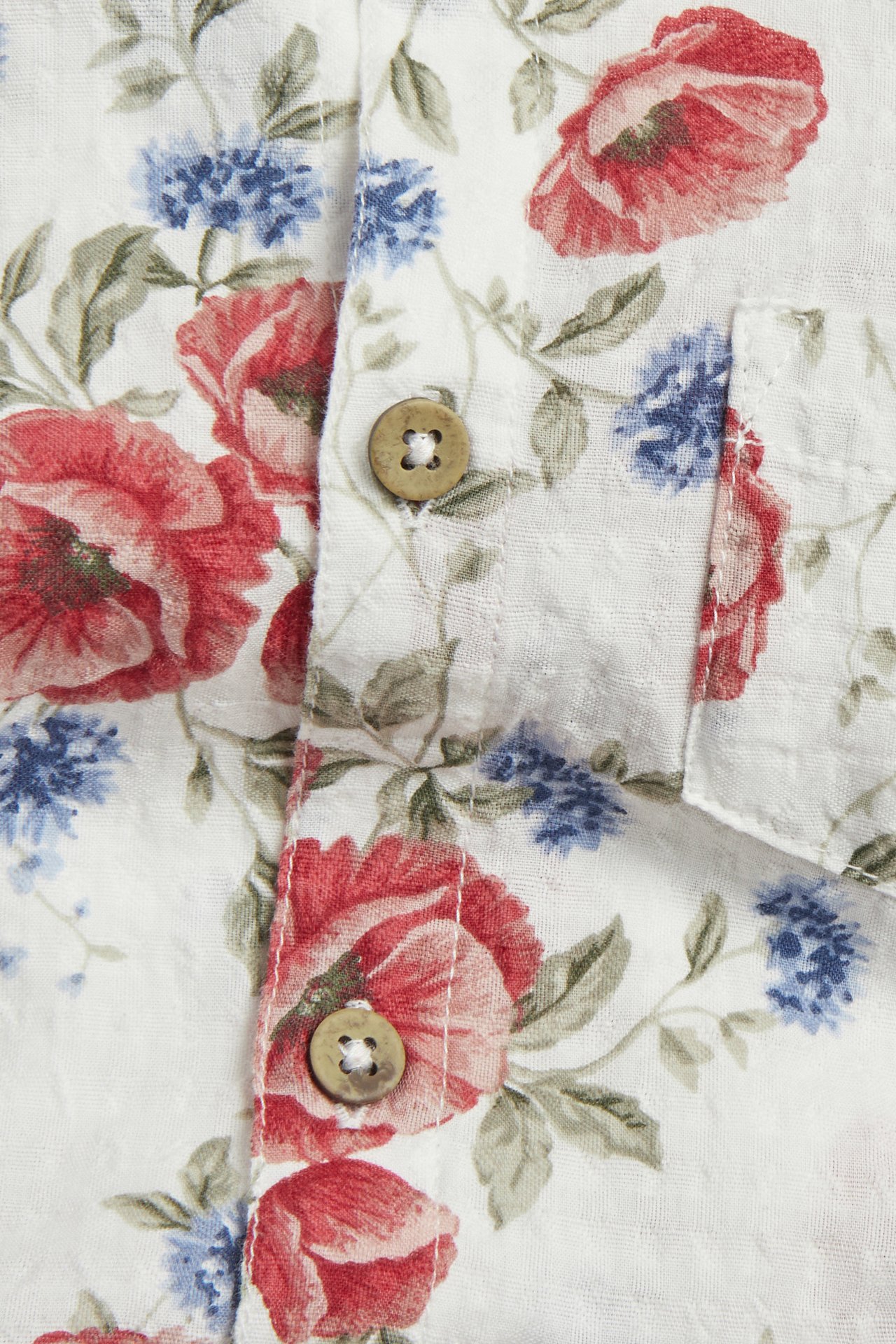 Nahaufnahme: Off-white Baumwoll-Shirtbody, Blumenmuster rot/blau, braune Knöpfe, Brusttasche.