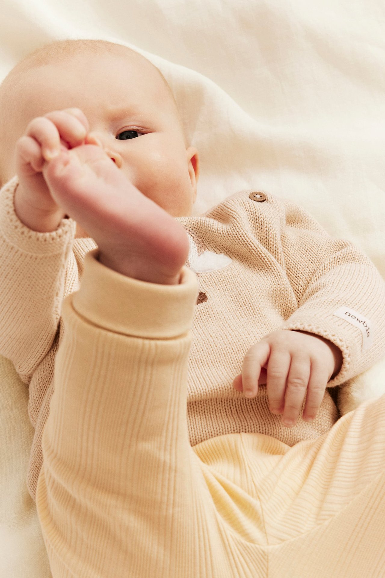 Close-up of a baby wearing a light beige knitted sweater with embroidery and matching ribbed pants.