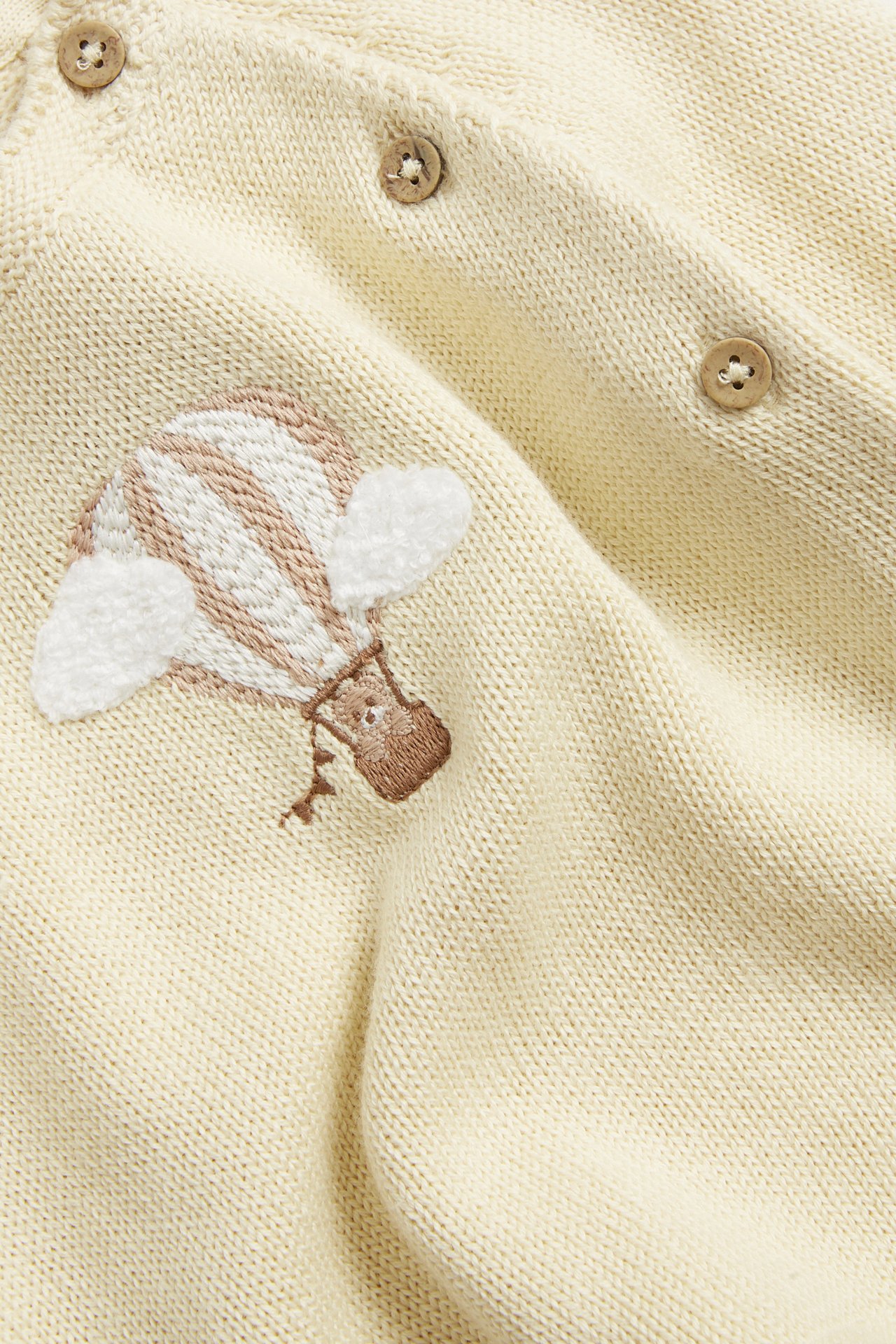 Close-up of a baby's light yellow fine-knit cotton cardigan with hot air balloon embroidery and wooden buttons.