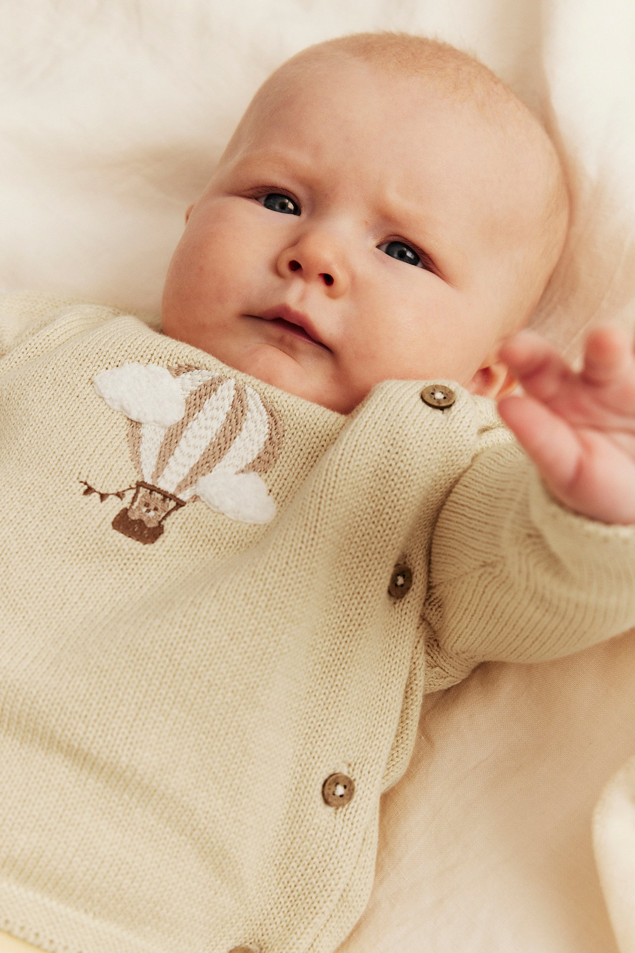 Nahaufnahme: Baby trägt hellgelbe Baumwollstrickjacke mit Heißluftballon-Stickerei und seitlichen Knöpfen.